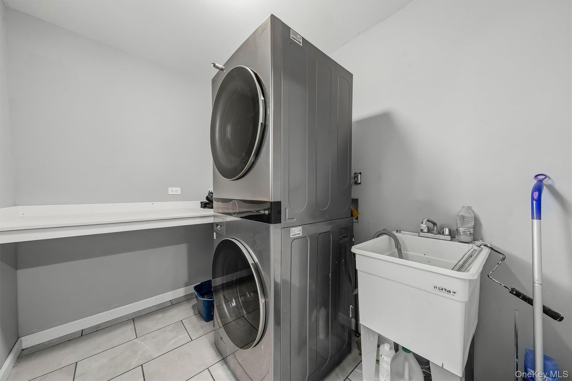 Laundry area featuring a stacked washer and dryer, utility sink with faucet, and light-toned tile flooring