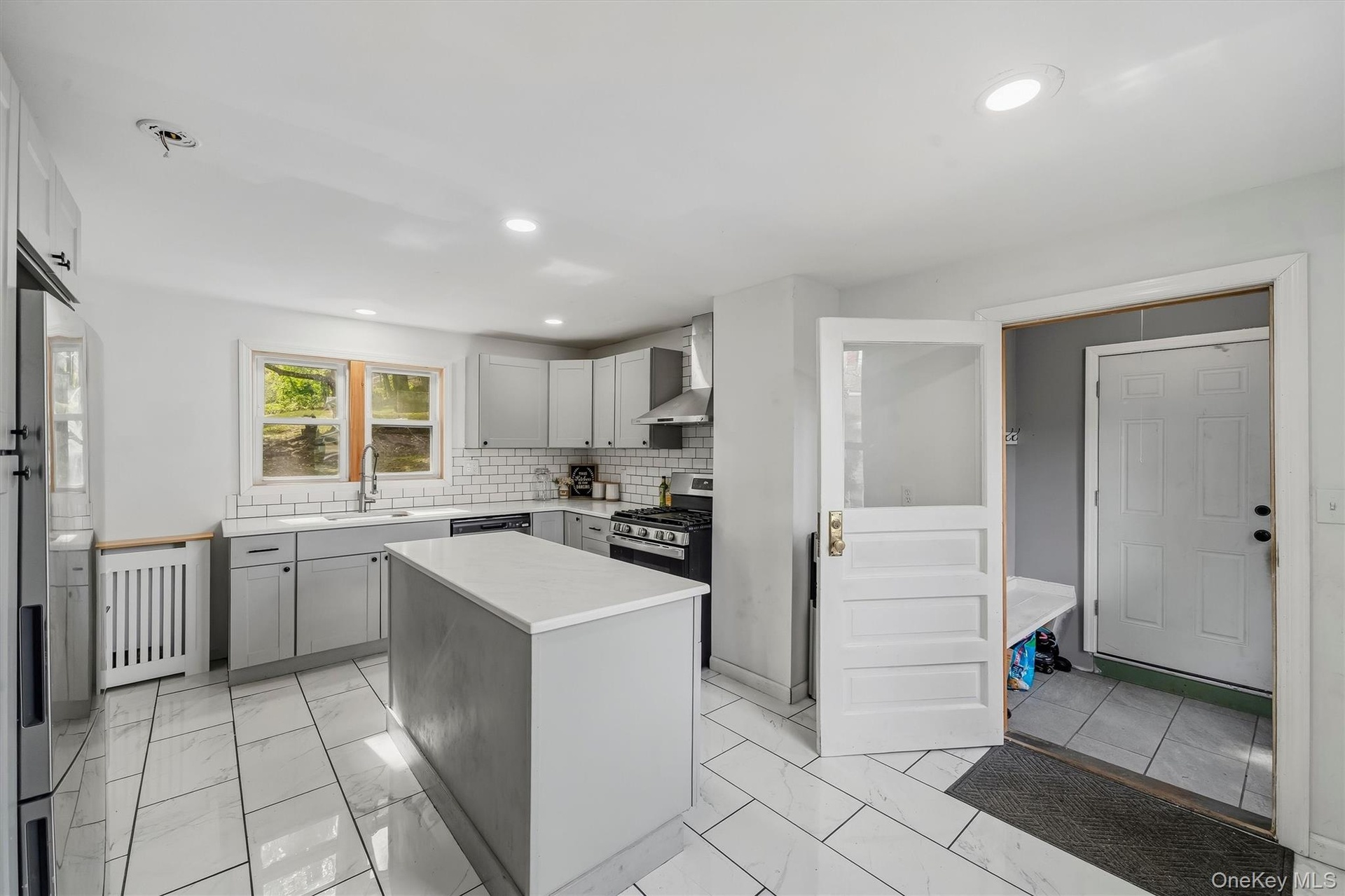 Kitchen featuring an island with a light-toned countertop, subway tile backsplash, stainless steel appliances, and recessed lighting
