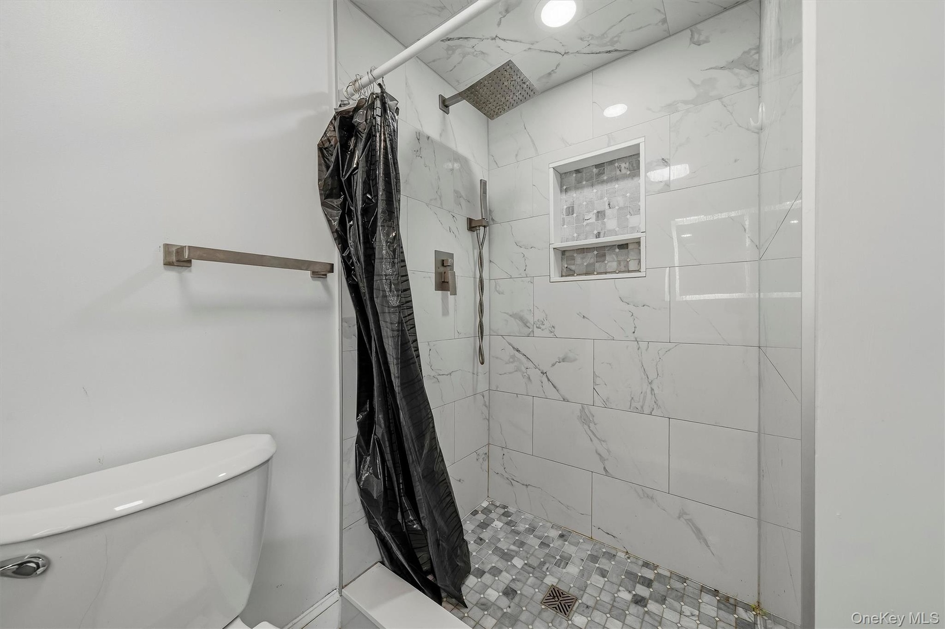 Shower featuring white marble-look subway tile, mosaic tile shower floor, built-in shower niche, and a rain shower head with an additional handheld sh