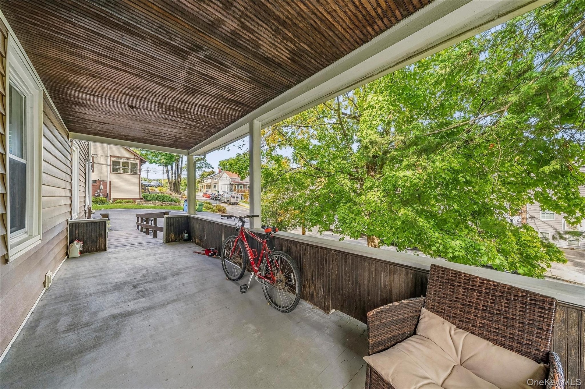 Covered porch featuring a wood-plank ceiling, concrete flooring, and slatted wood railing