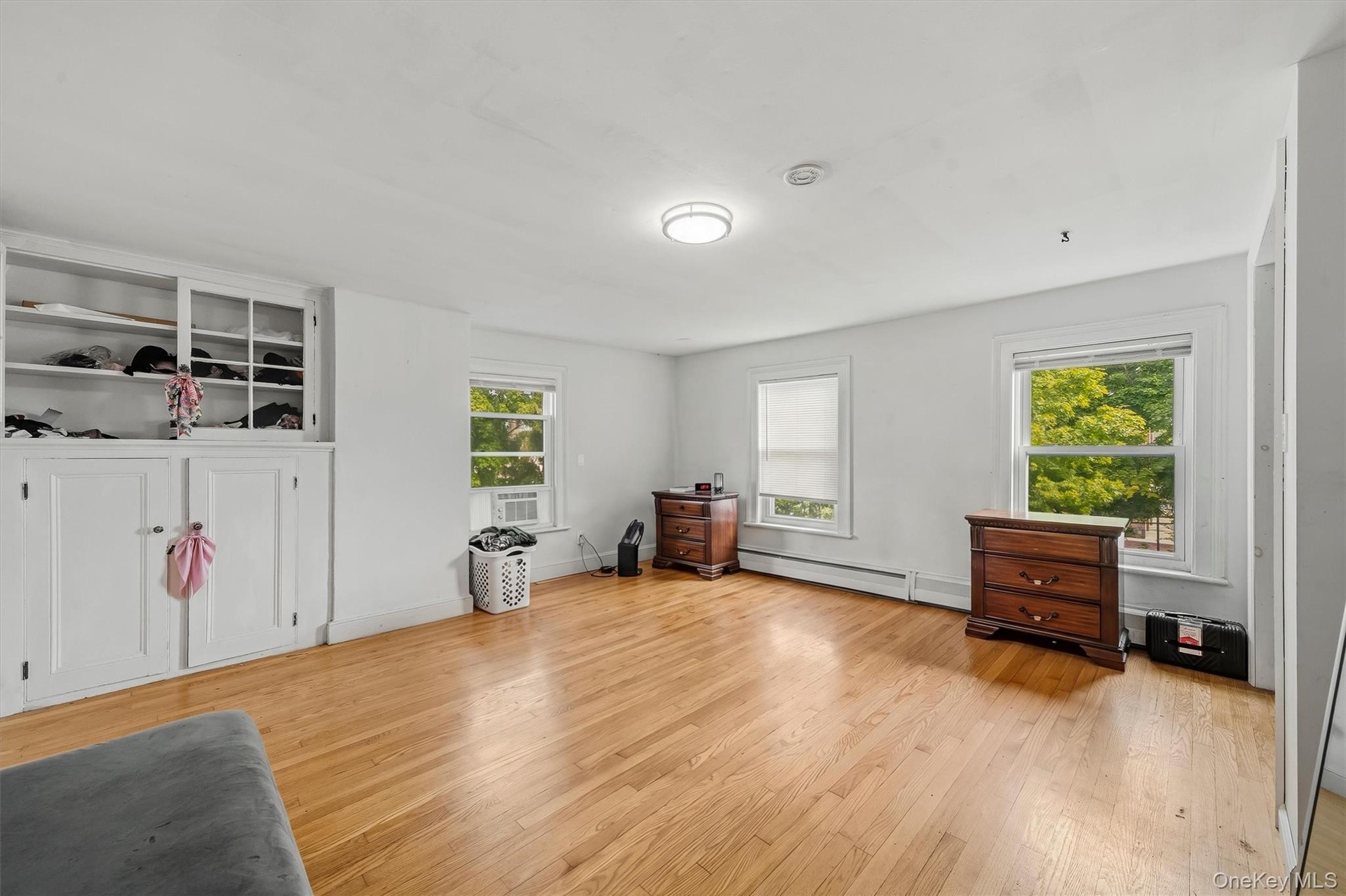 Large bedroom with hardwood floors, multiple windows, and built-in storage.