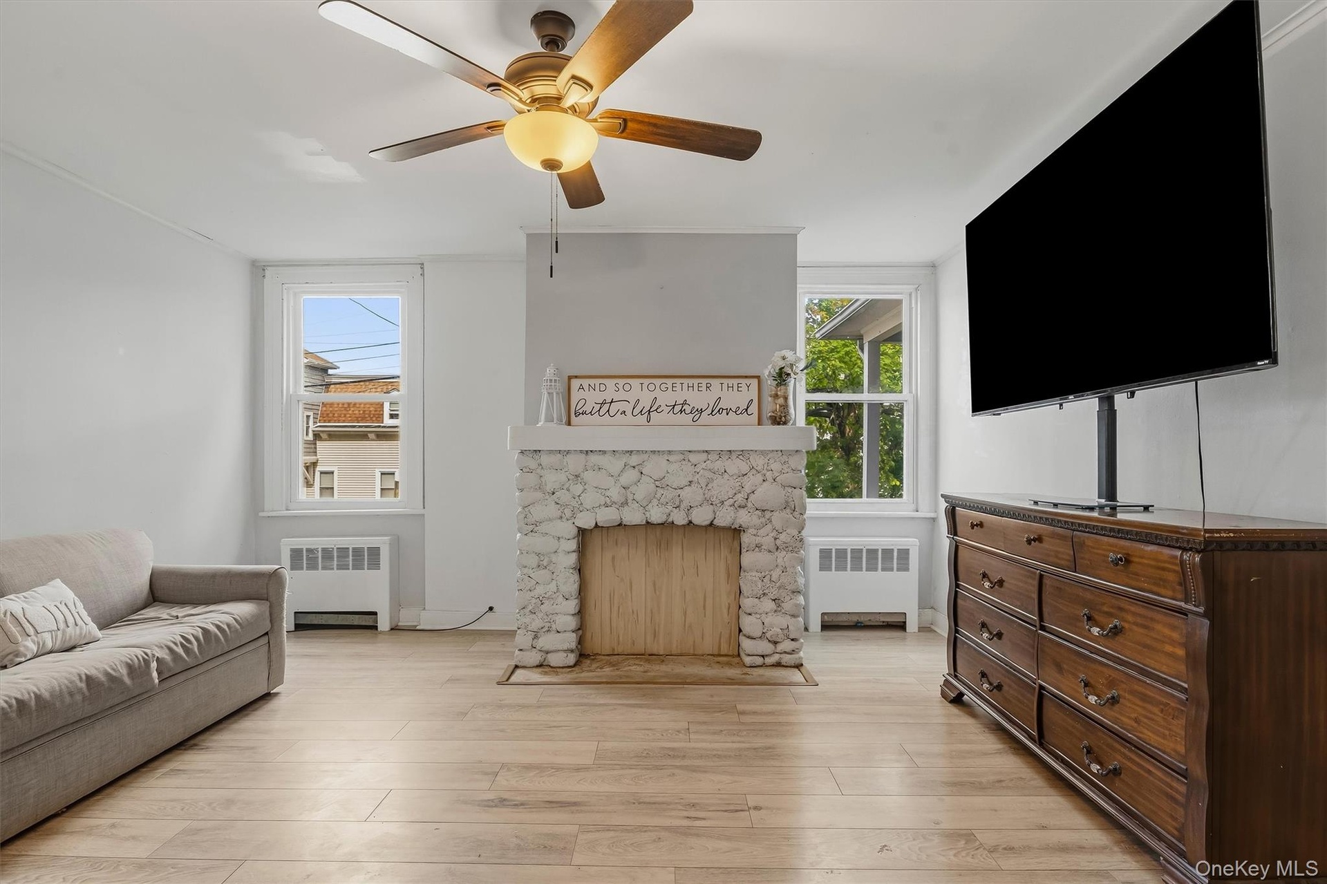 Light wood-finish flooring, a white stone-clad fireplace, and multiple windows