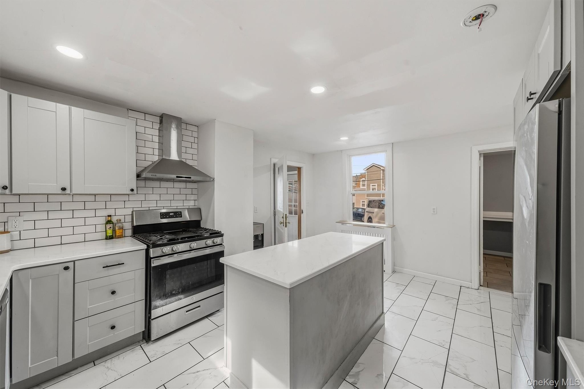 Modern kitchen featuring white subway tile backsplash, stainless steel range and hood, light-toned cabinetry, a central island, and large format floor
