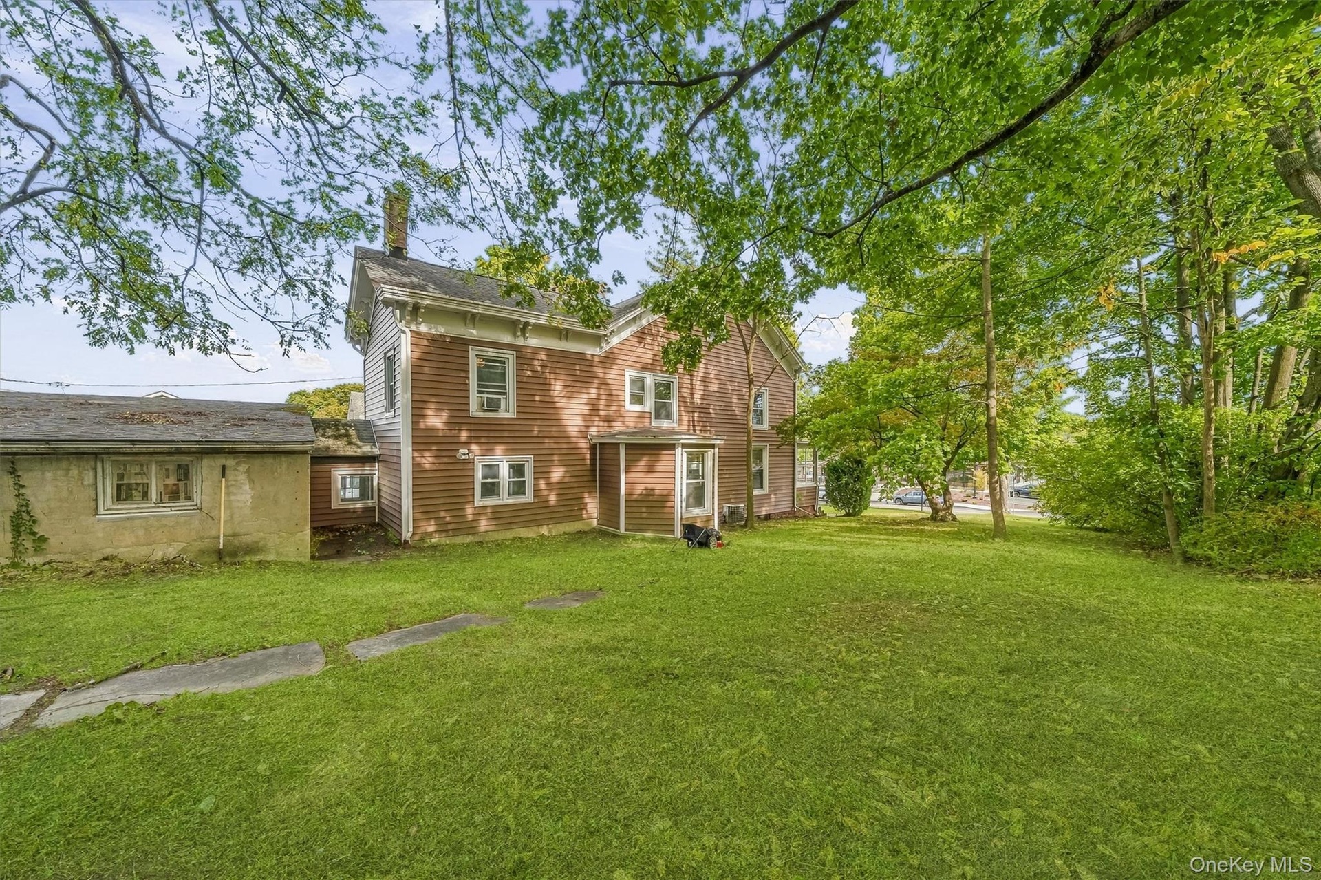 Expansive green lawn with mature trees and a multi-level structure featuring red siding and white trim