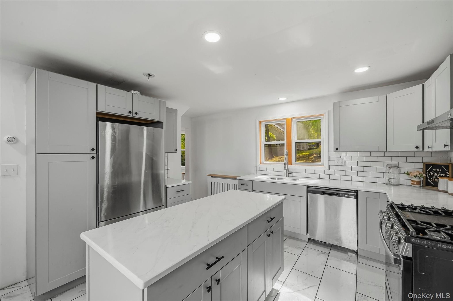 Kitchen featuring gray shaker-style cabinetry, a central island with a light-toned countertop, a subway tile backsplash, and stainless steel appliance