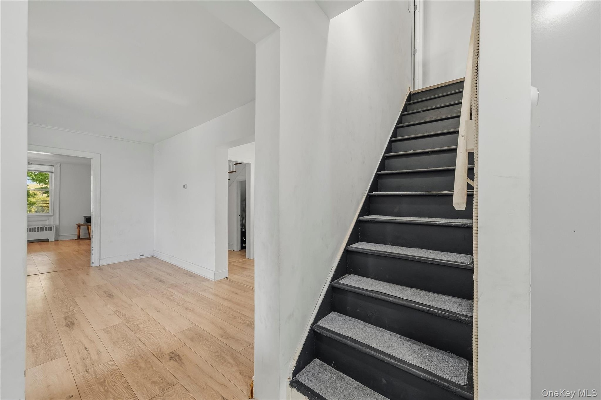 Wood-finish flooring, white wall finishes, dark-painted staircase with textured treads, and multiple doorways
