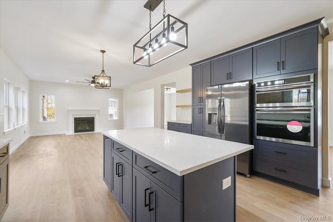 Kitchen with appliances with stainless steel finishes, decorative light fixtures, a center island, and light hardwood / wood-style flooring