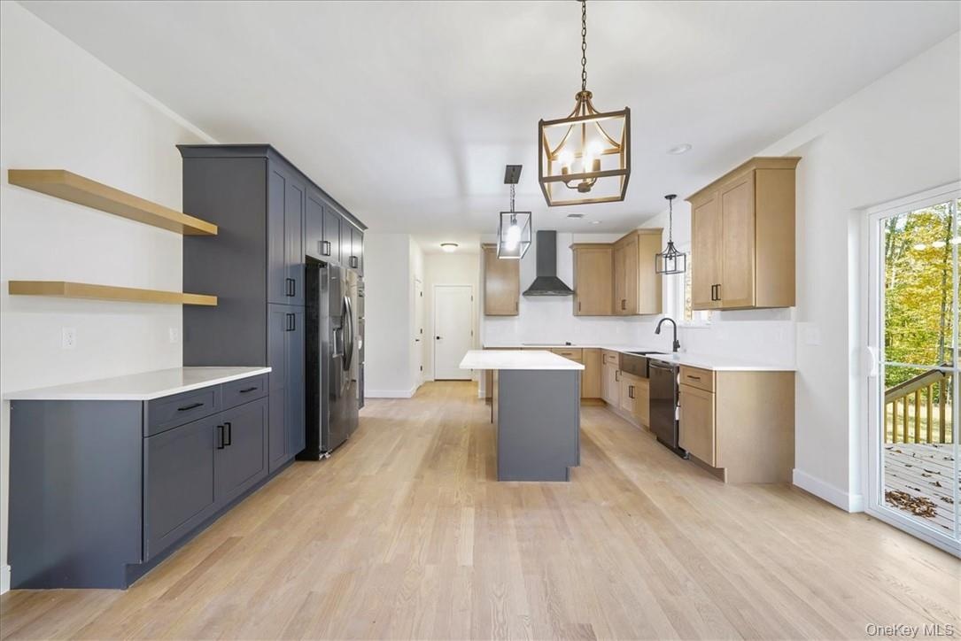 Kitchen with a center island, stainless steel appliances, light hardwood / wood-style floors, wall chimney range hood, and decorative light fixtures