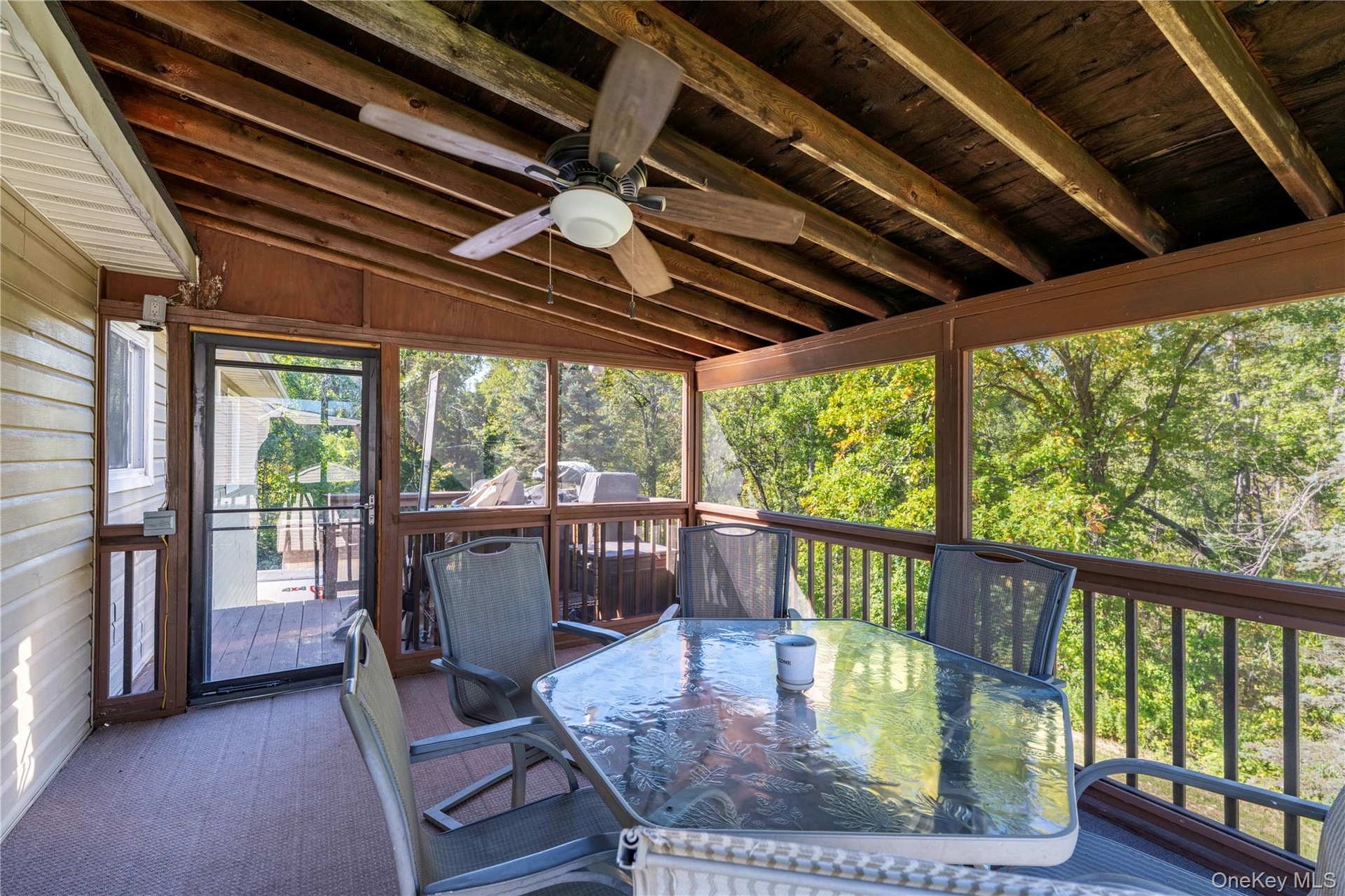 Screened-in deck featuring a wood-finish ceiling with exposed beams, ceiling fan, and a light wood-finish railing system