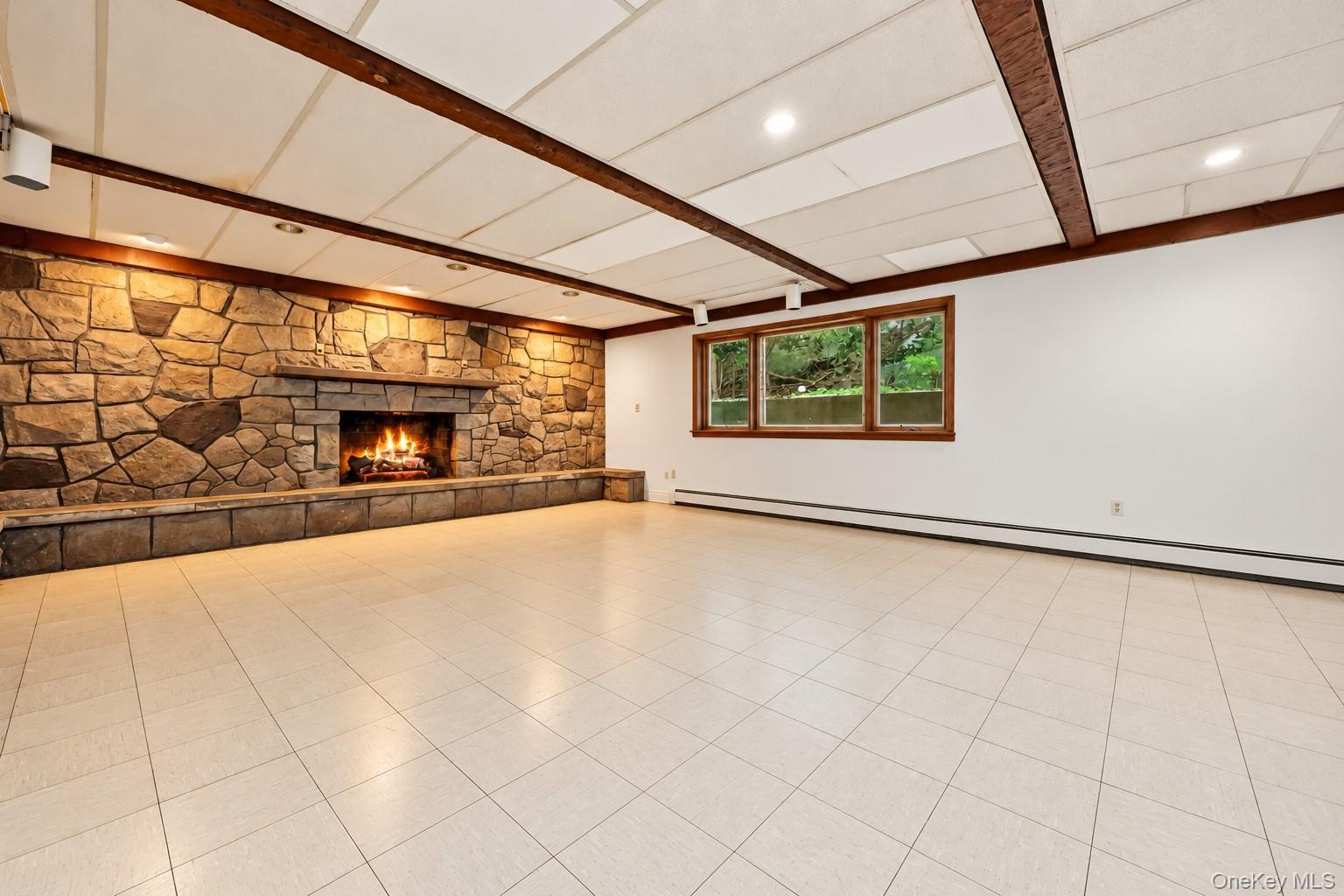 Lower level family room has stone fireplace and beamed ceiling with large windows and acoustic ceiling.  Extraneous objects removed.