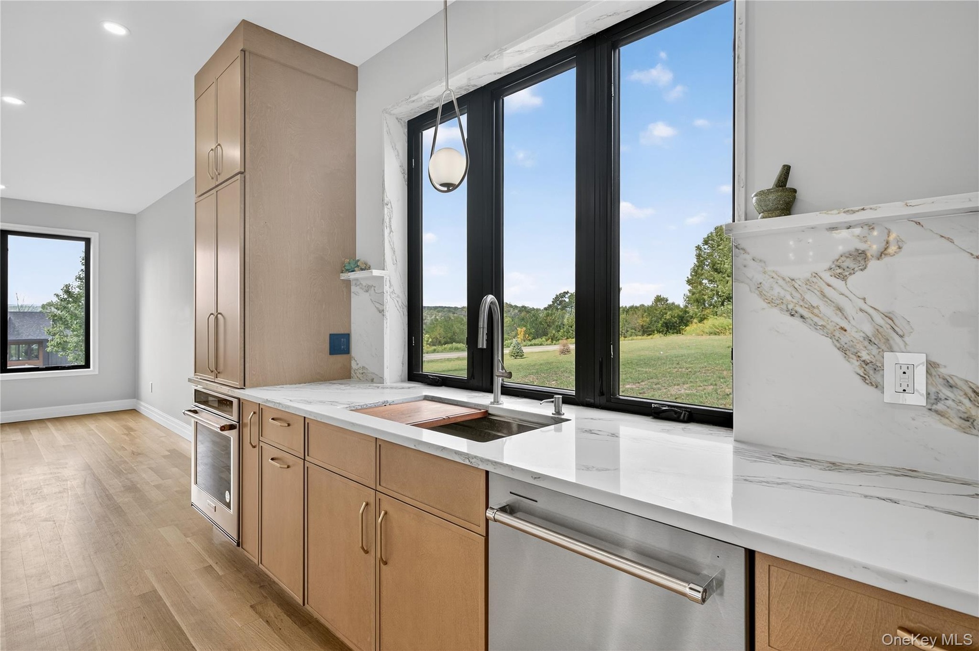 Kitchen with light stone counters, appliances with stainless steel finishes, light wood-style floors, pendant lighting, and light brown cabinetry