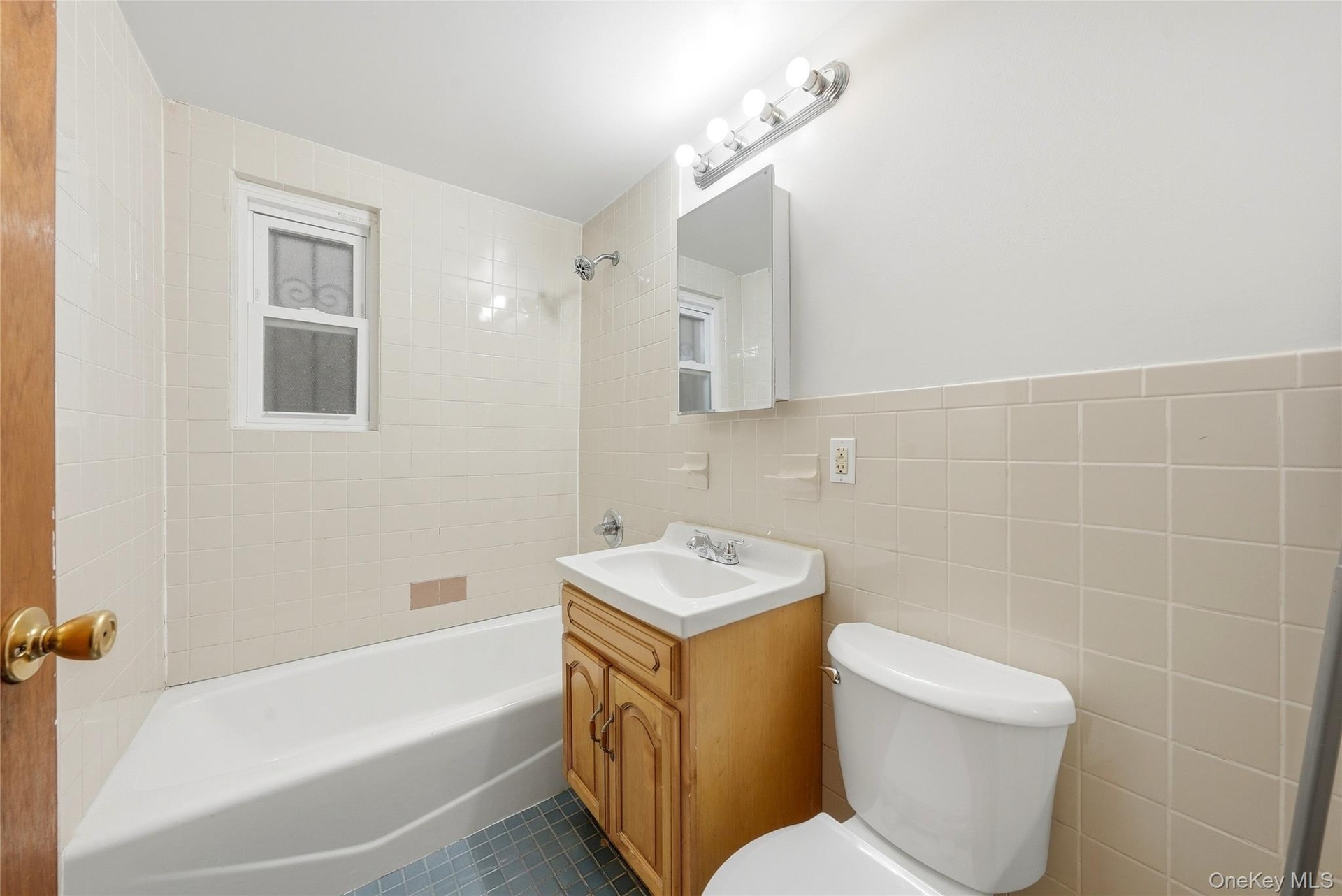 Bathroom featuring a full bathtub, window, vanity with integrated sink, wall-mounted medicine cabinet, and tiled walls