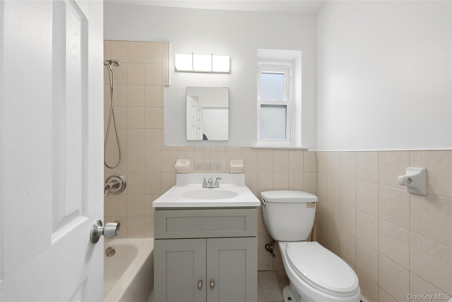 Bathroom featuring a single window, tiled walls, a vanity with a single sink, and a shower-tub combination