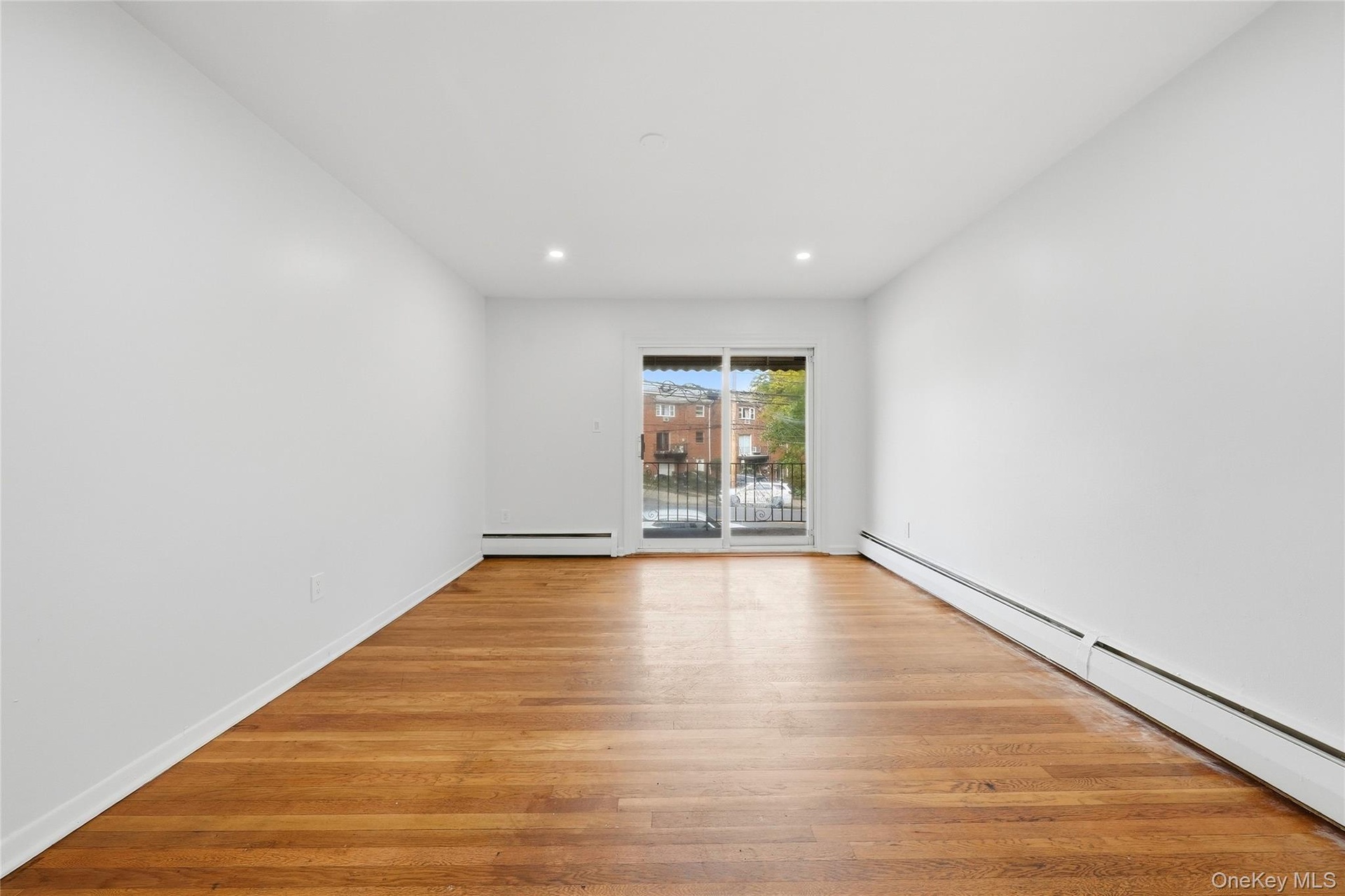 Hardwood flooring, recessed lighting, white walls, baseboard heating, and sliding glass doors