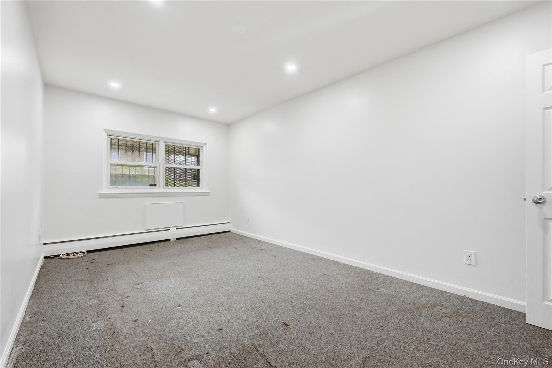 Recessed ceiling lighting, a window with security bars, and baseboard heating