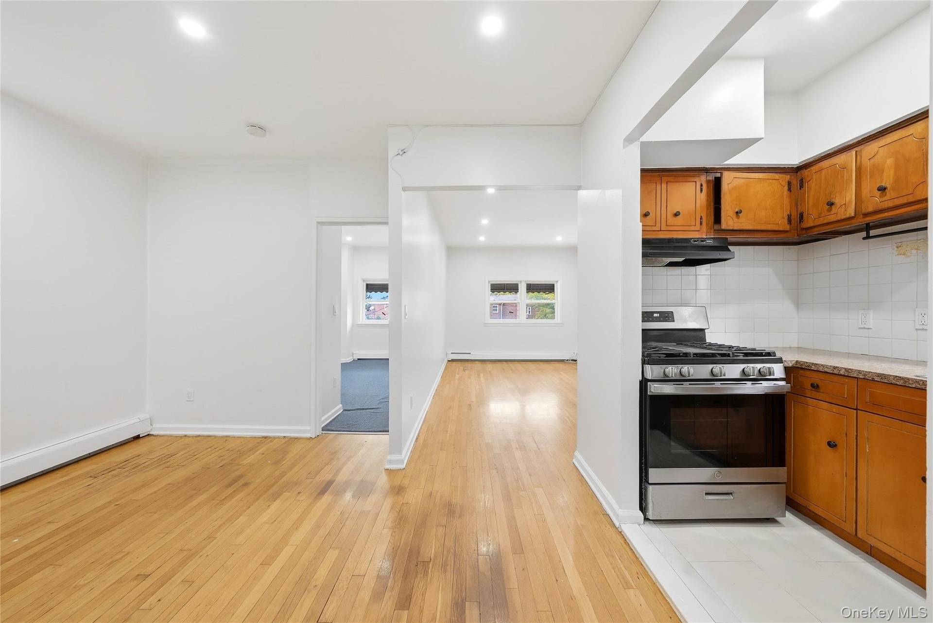 Hardwood flooring, recessed lighting, stainless steel gas range, wood cabinetry, and tiled backsplash