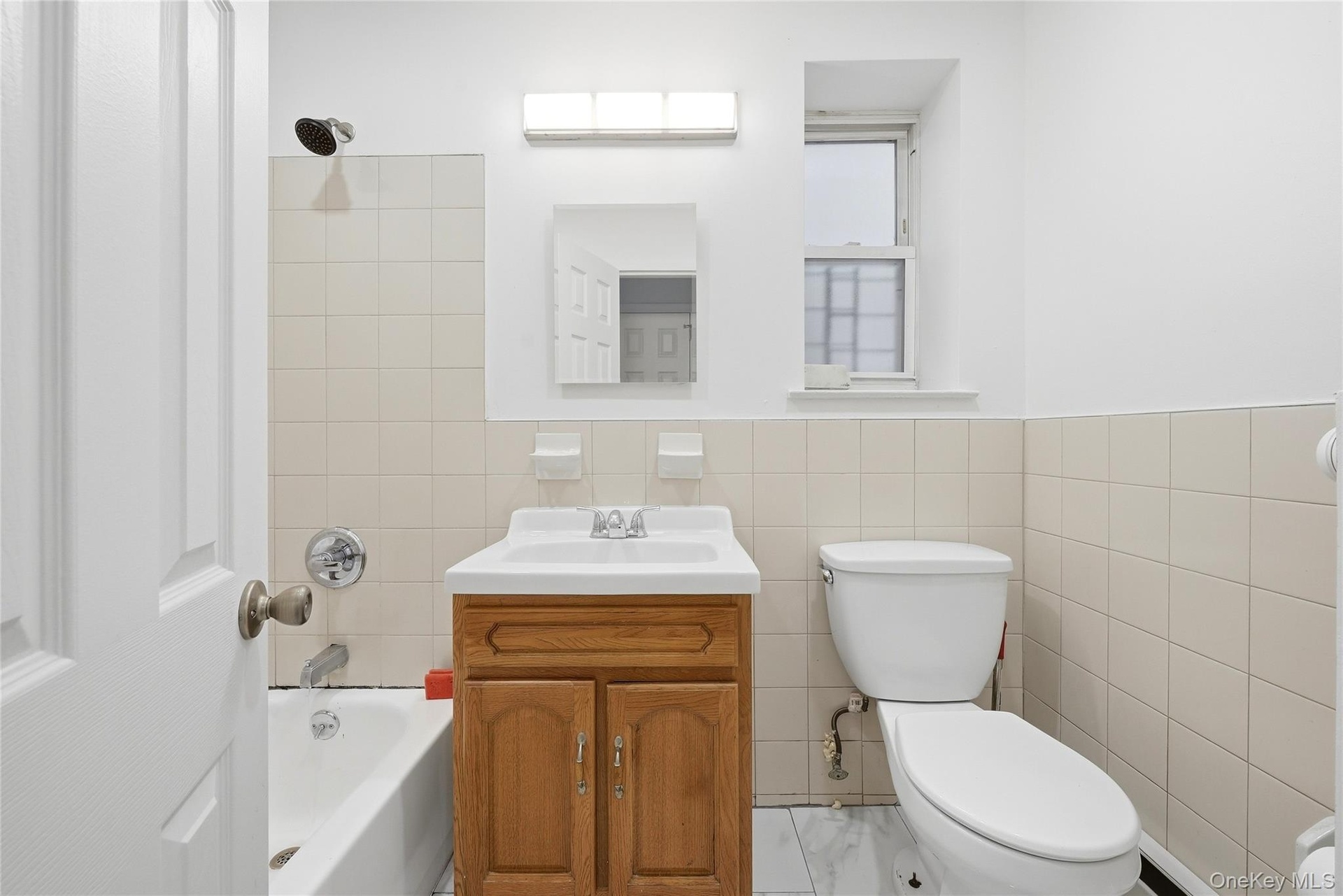 Bathroom with a wood-finish vanity, integrated sink, tiled walls, and a white toilet