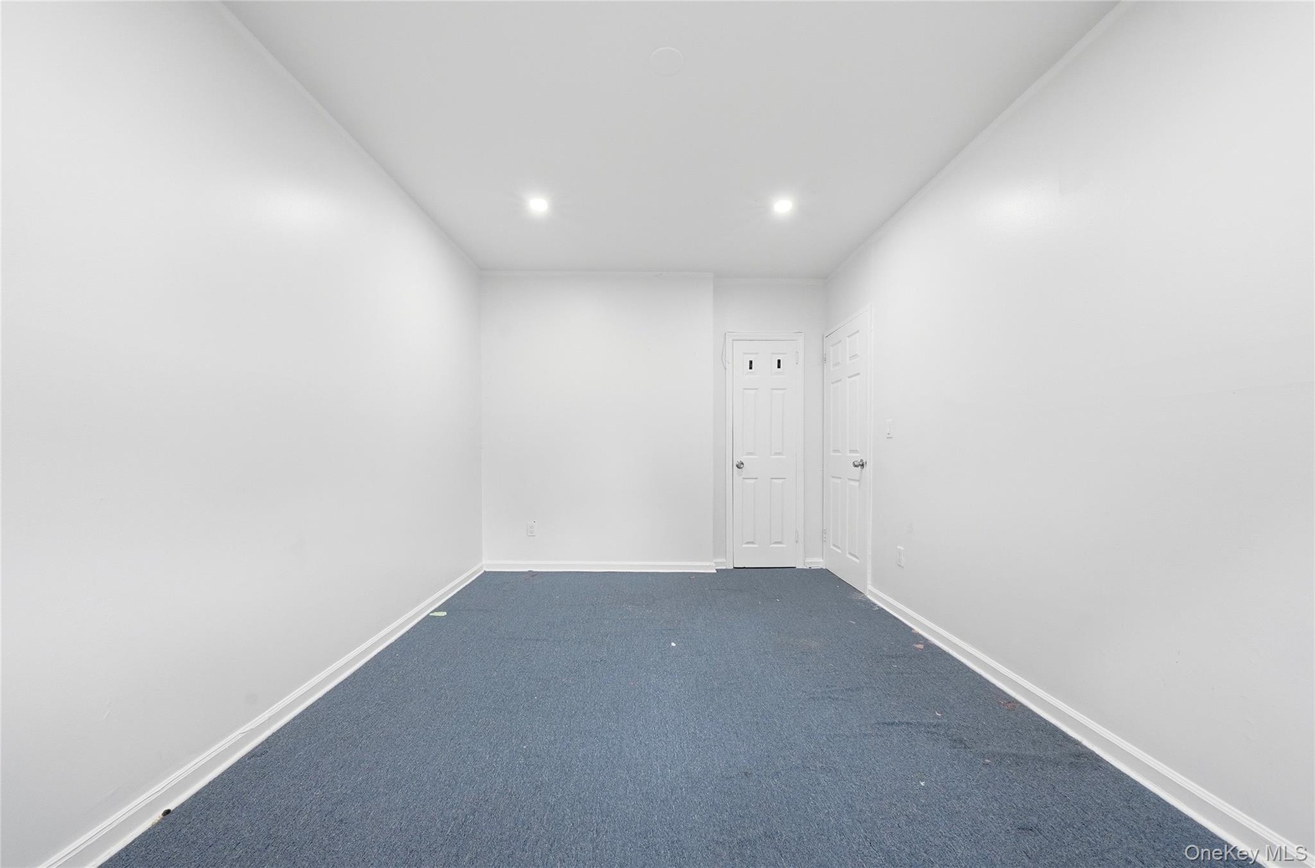 Recessed lighting illuminates the room, featuring white walls and a blue carpeted floor