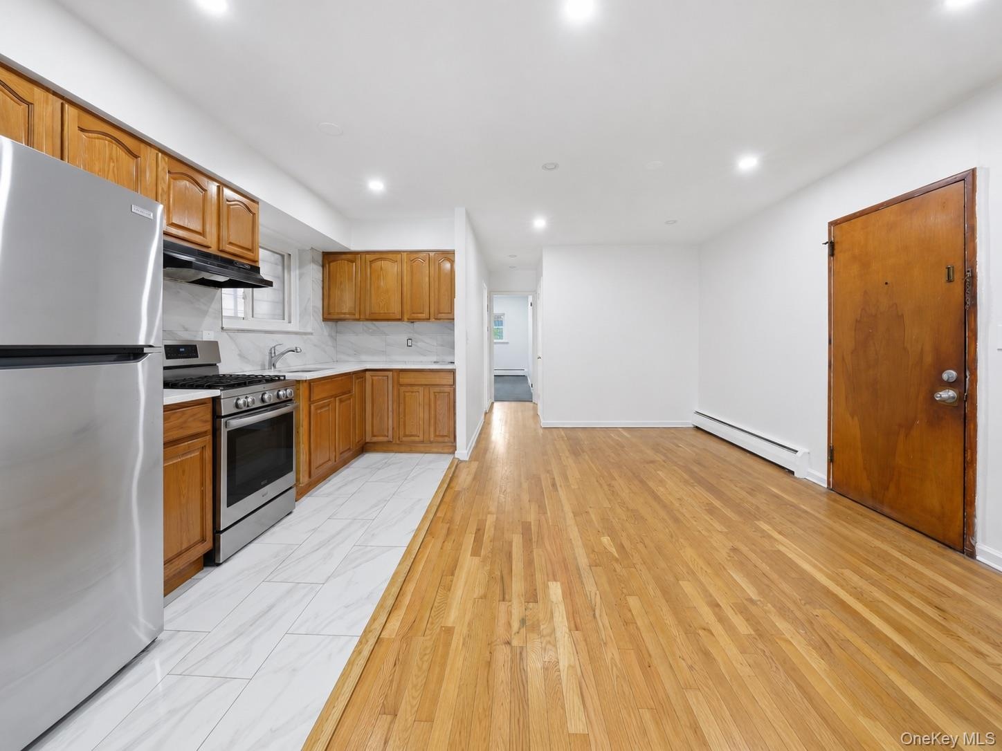 Open-concept living space featuring wood-finish flooring, recessed lighting, wood cabinetry, stainless steel appliances, and white tile flooring in th