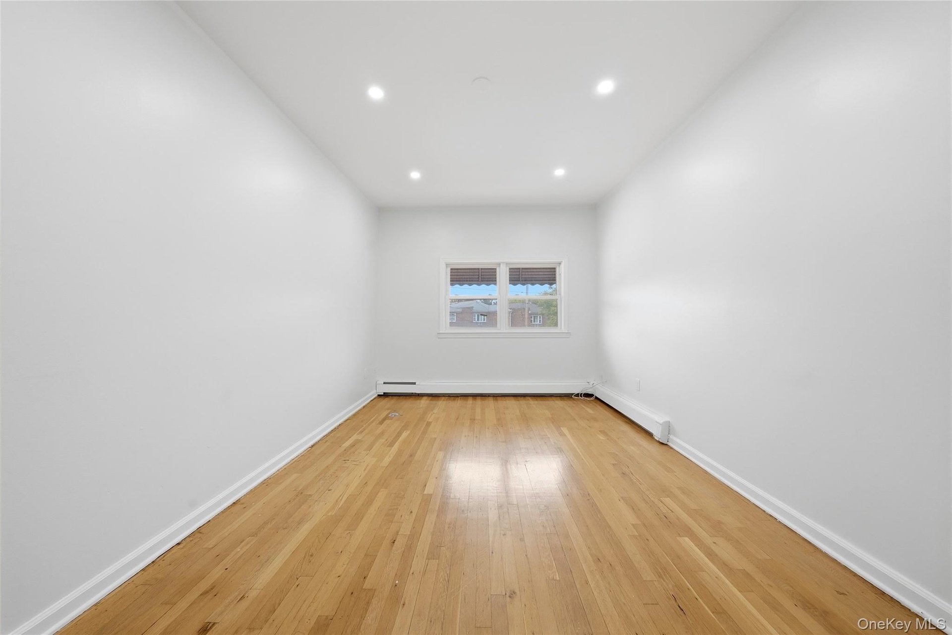 Hardwood flooring, recessed ceiling lighting, a window with an awning, and pristine white walls