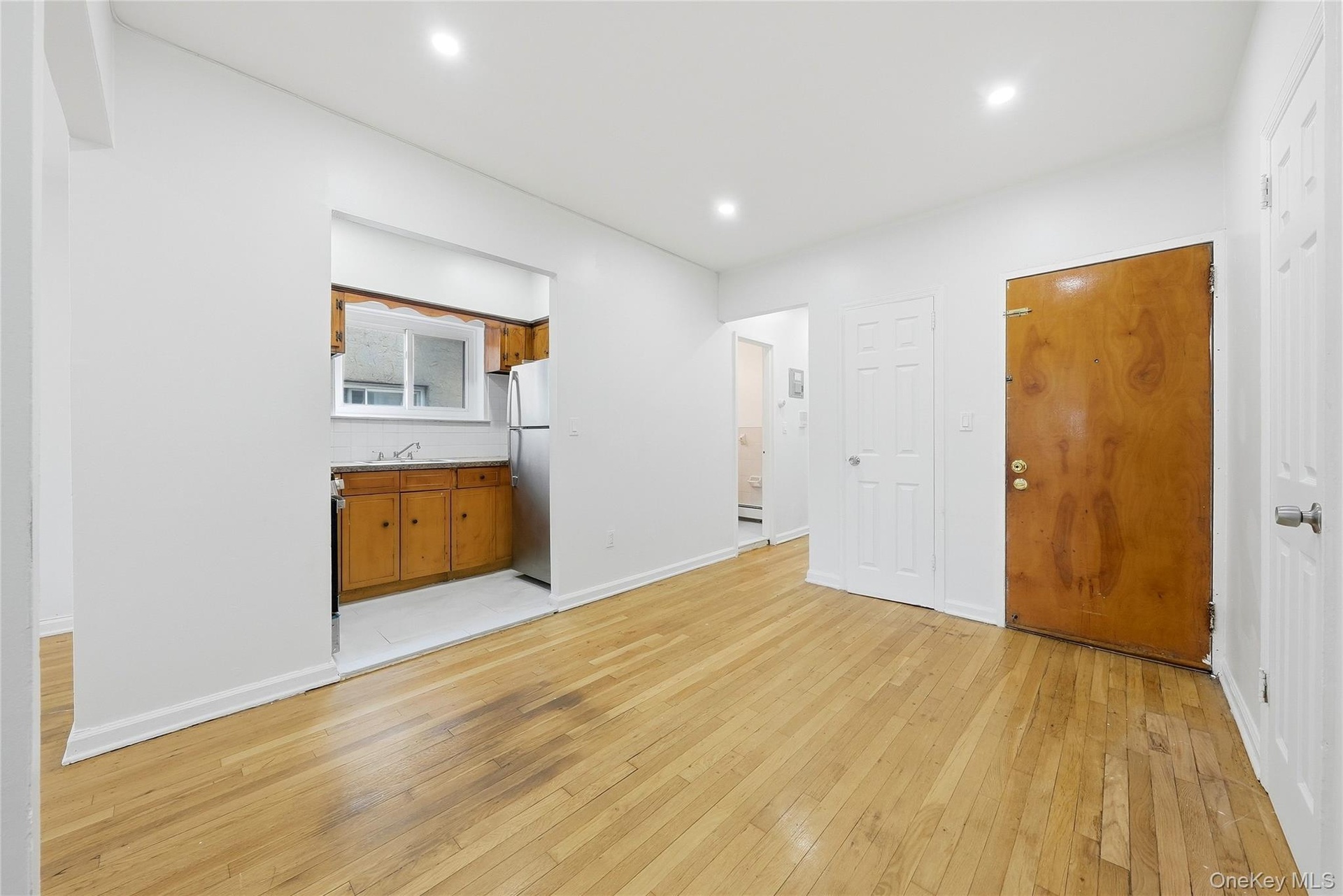 Wood-finish flooring throughout, recessed lighting, and a kitchen alcove with wood cabinetry and a stainless steel refrigerator
