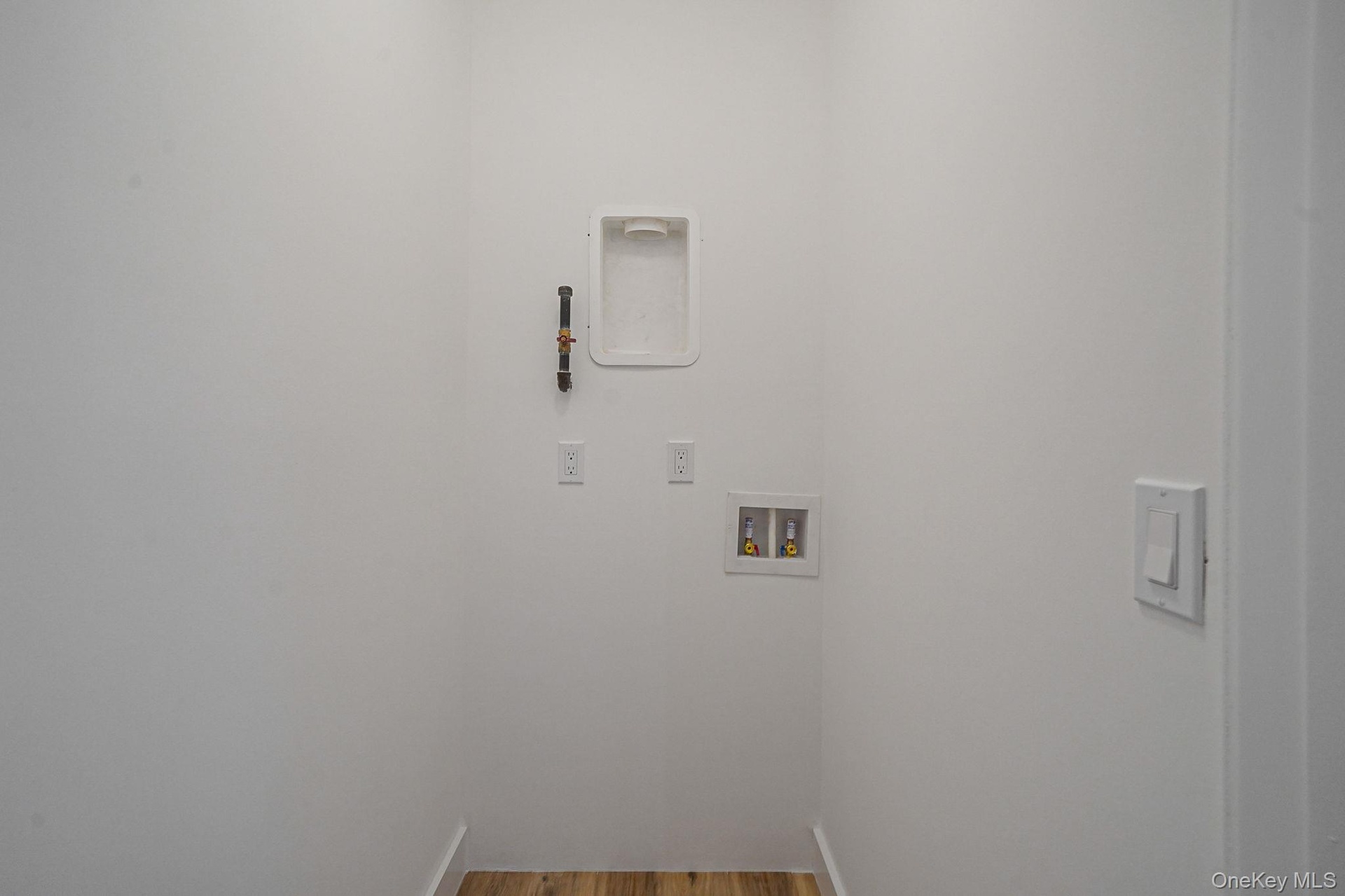 Washroom with hookup for a washing machine and wood finished floors