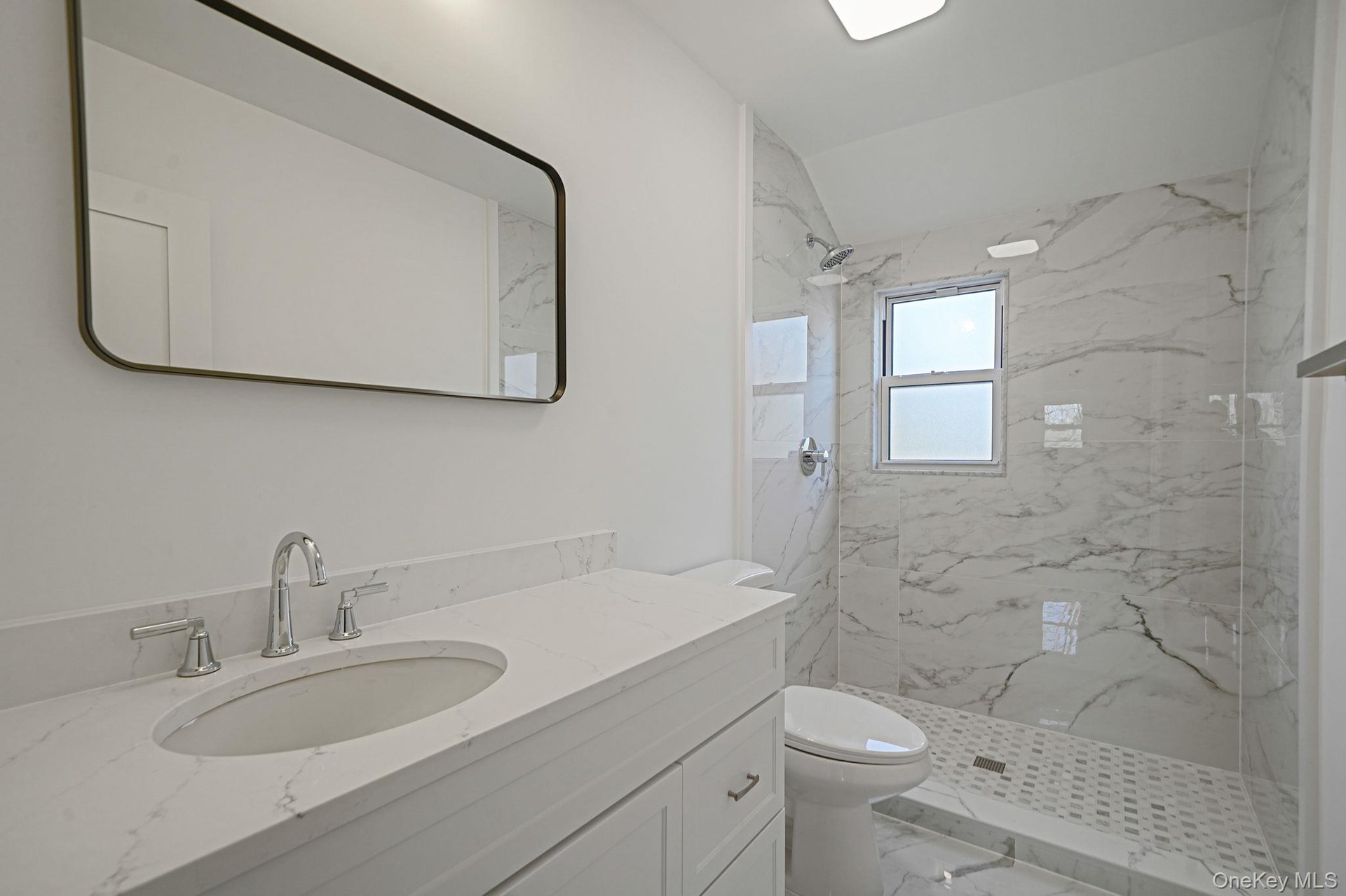 Full bath with marble look tile flooring, toilet, vanity, and a marble finish shower