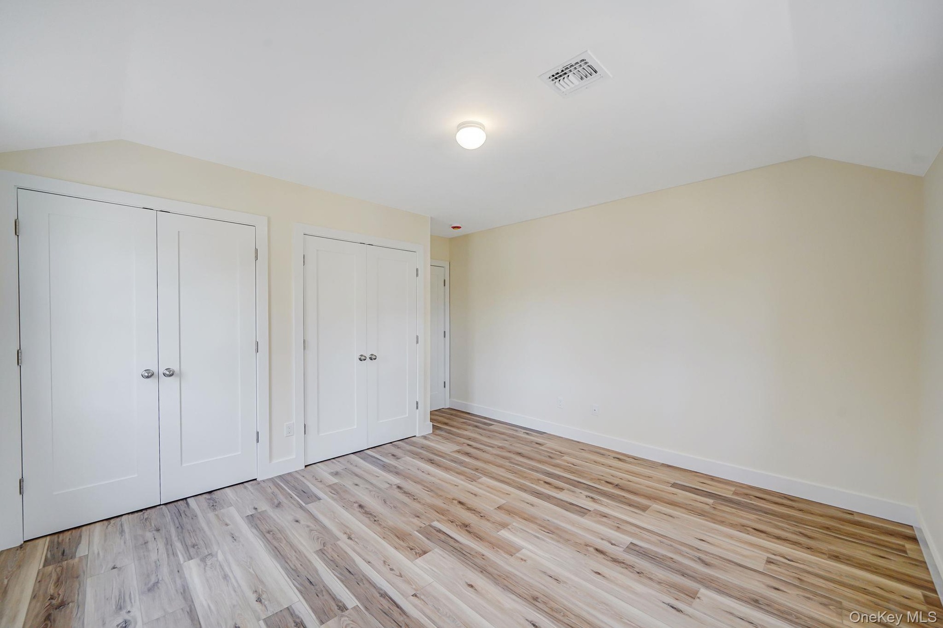 Unfurnished bedroom with multiple closets, vaulted ceiling, light wood-style flooring, and baseboards