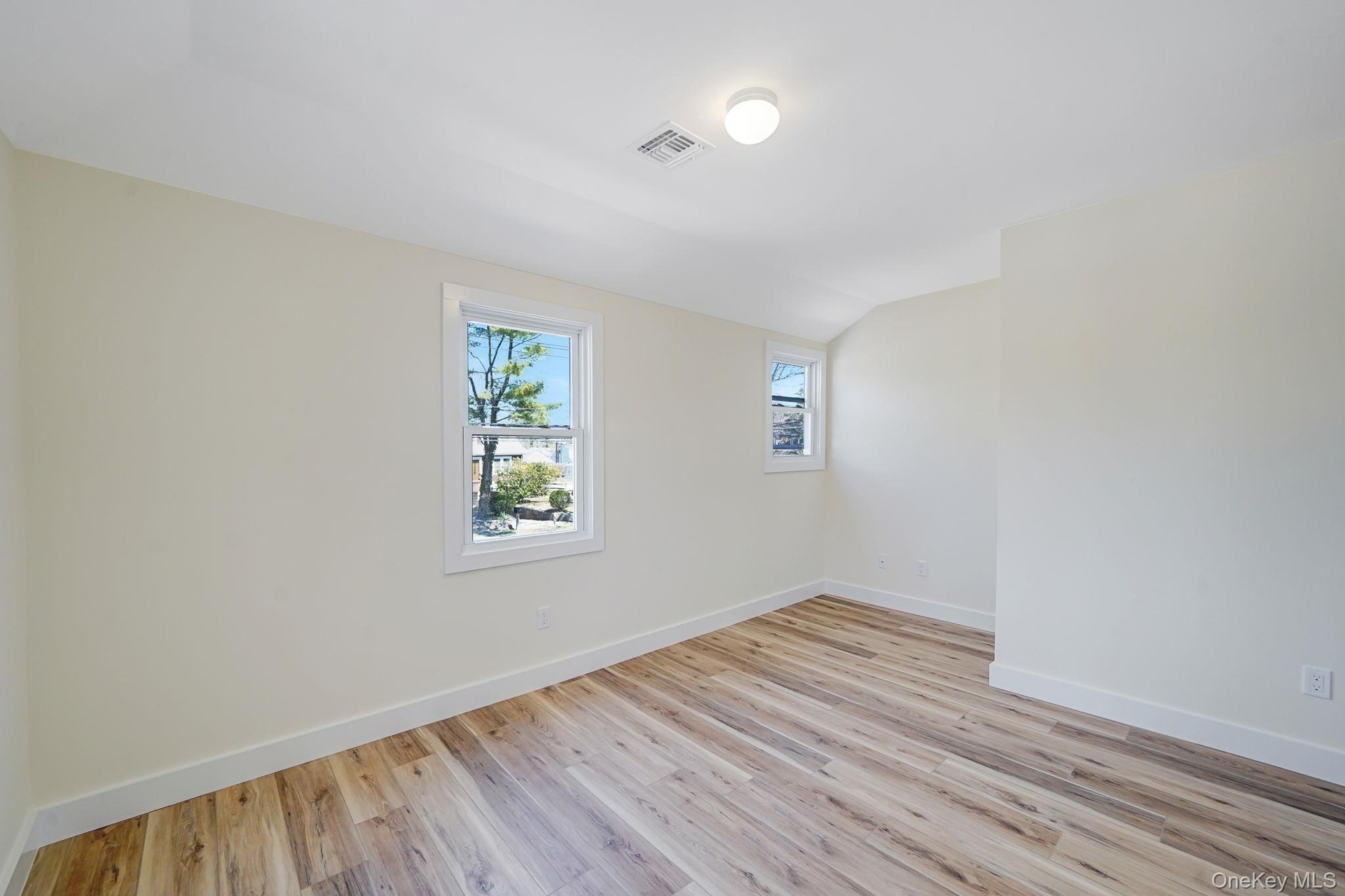 Unfurnished room featuring baseboards, light wood-style floors, and lofted ceiling