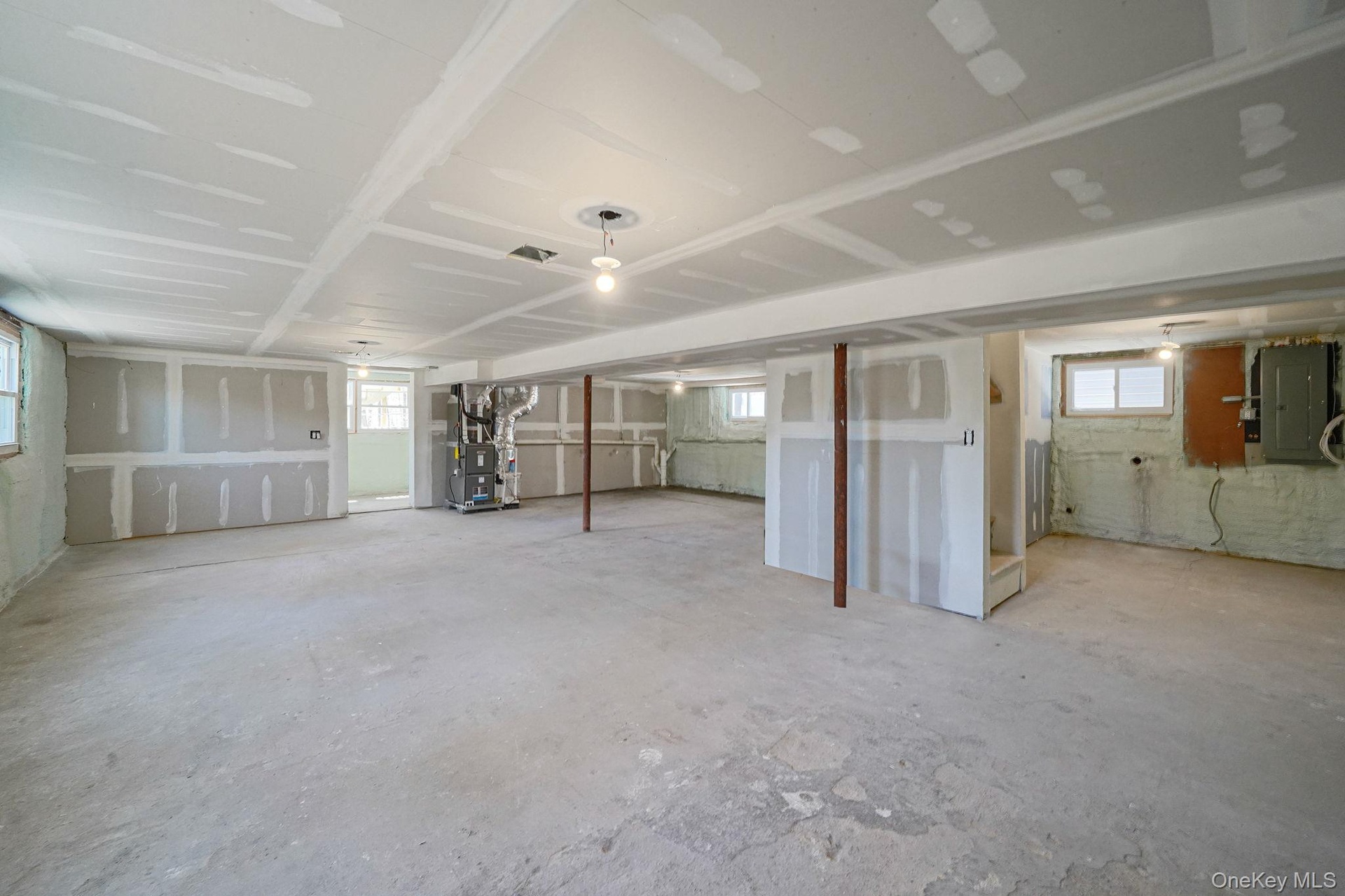 Basement with electric panel, heating unit, and healthy amount of natural light