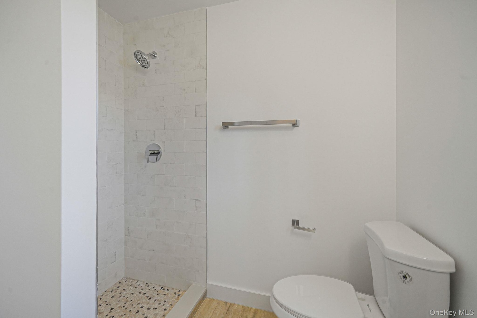 Bathroom with toilet, a tile shower, and wood finished floors