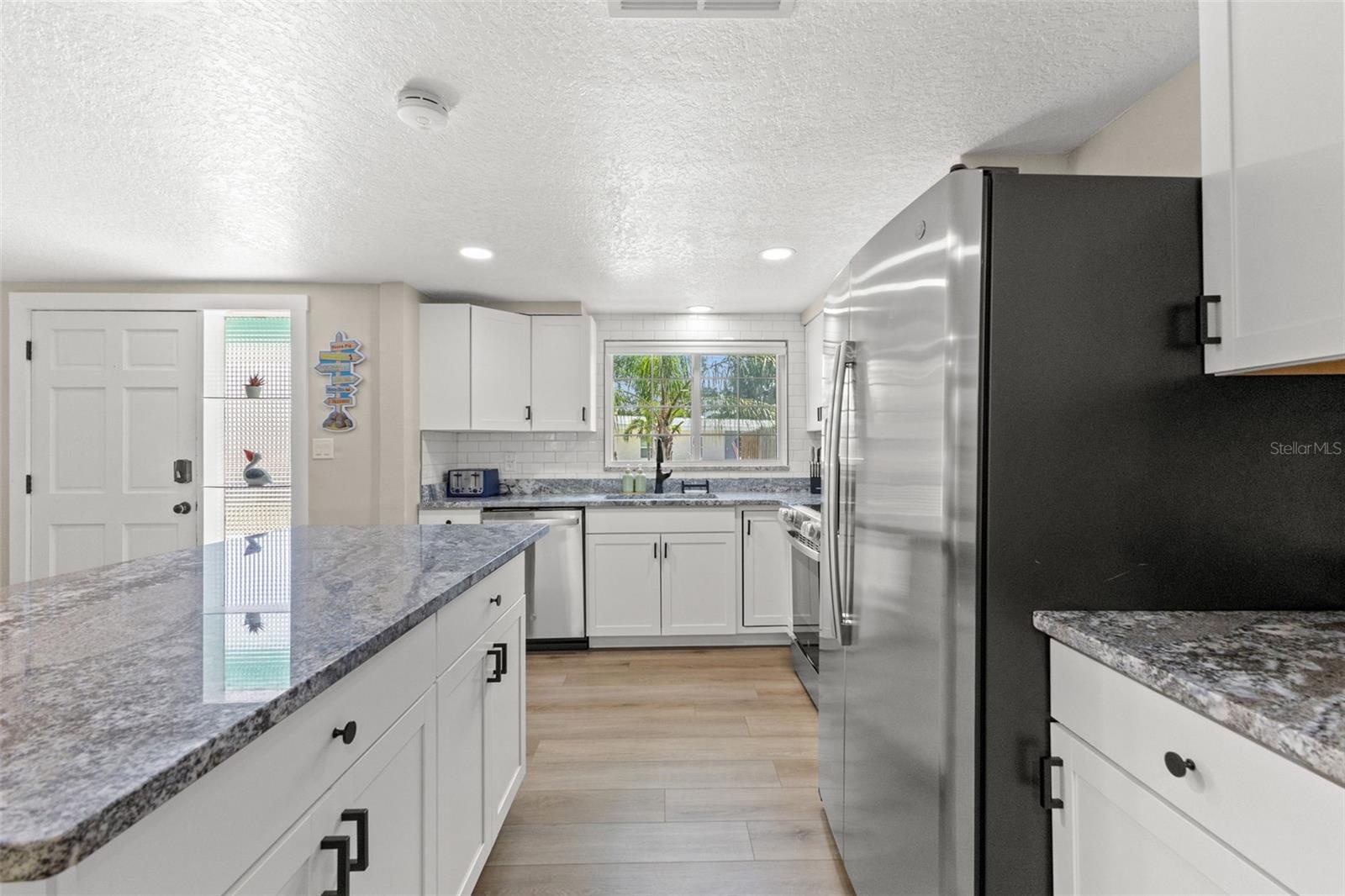 Another view highlights the kitchen’s extensive cabinetry, stainless steel appliances, granite surfaces, and luxury vinyl plank flooring.