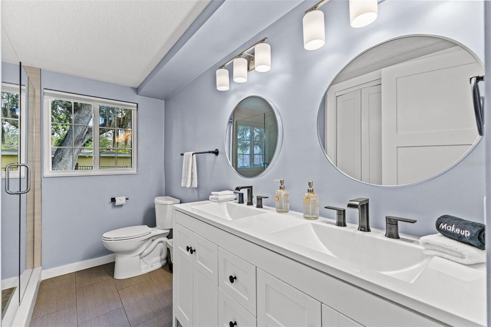 Updated bathroom with dual sinks, modern fixtures, generous vanity storage, and a glass-enclosed walk-in shower.