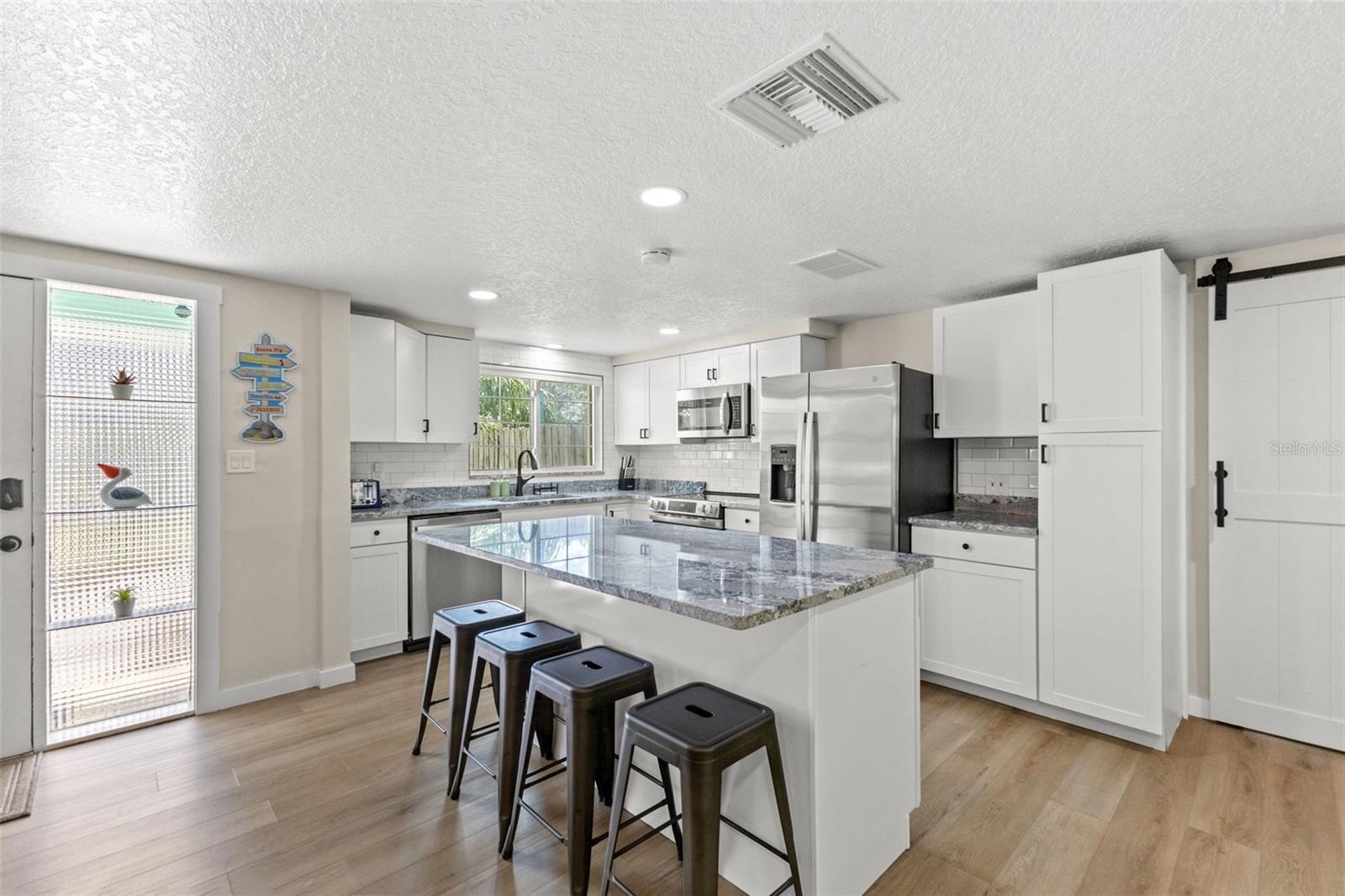Bright, renovated kitchen with a large center island, seating for four, stainless steel appliances, and plenty of cabinet storage.