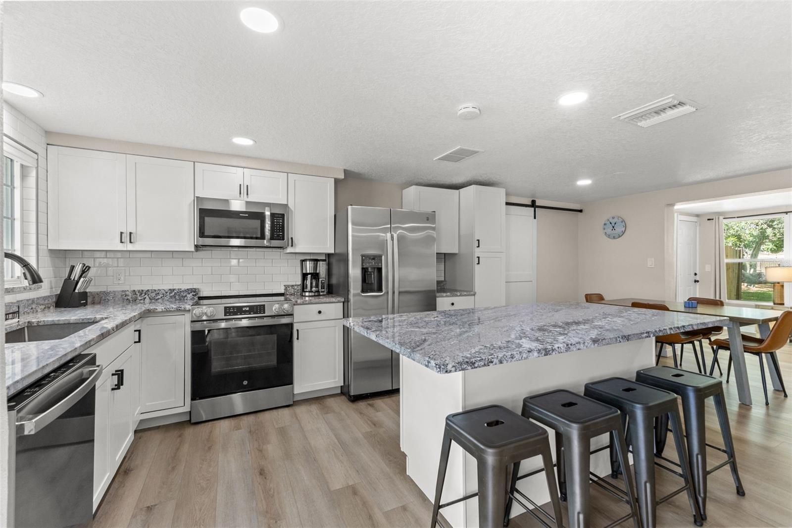 Renovated kitchen with white cabinetry, granite countertops, stainless steel appliances, and an oversized island with seating for four.