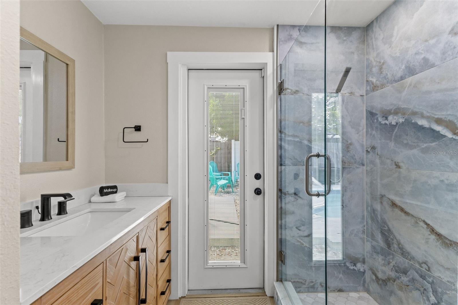 Updated bath features a modern vanity, quartz-style countertop, black fixtures, and a striking glass-enclosed tiled shower.