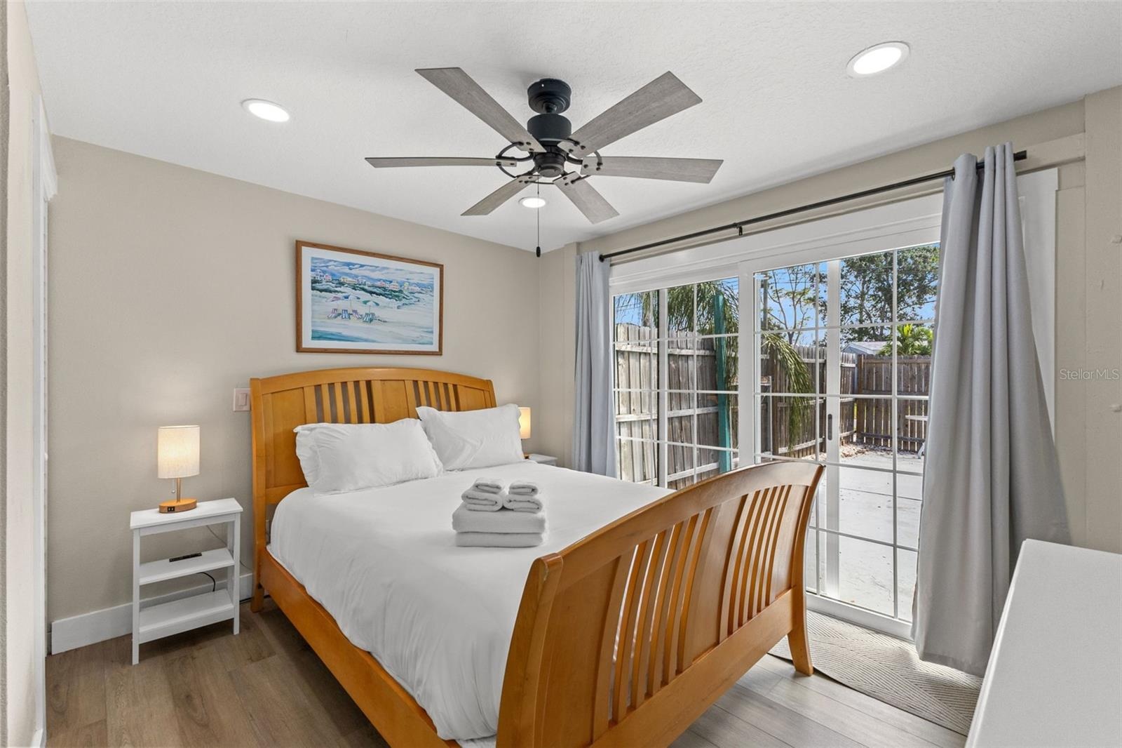 Owner's edroom with luxury vinyl plank flooring, ceiling fan, and sliding glass doors opening directly to the pool area.