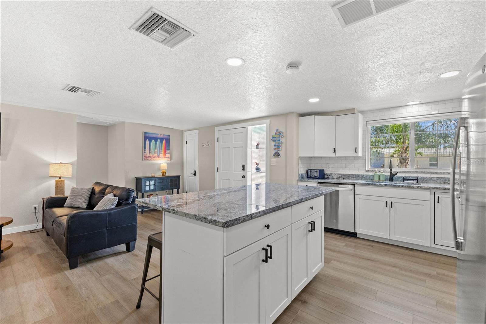 Generous granite-topped island adds abundant prep space, storage, and casual seating to the renovated kitchen.