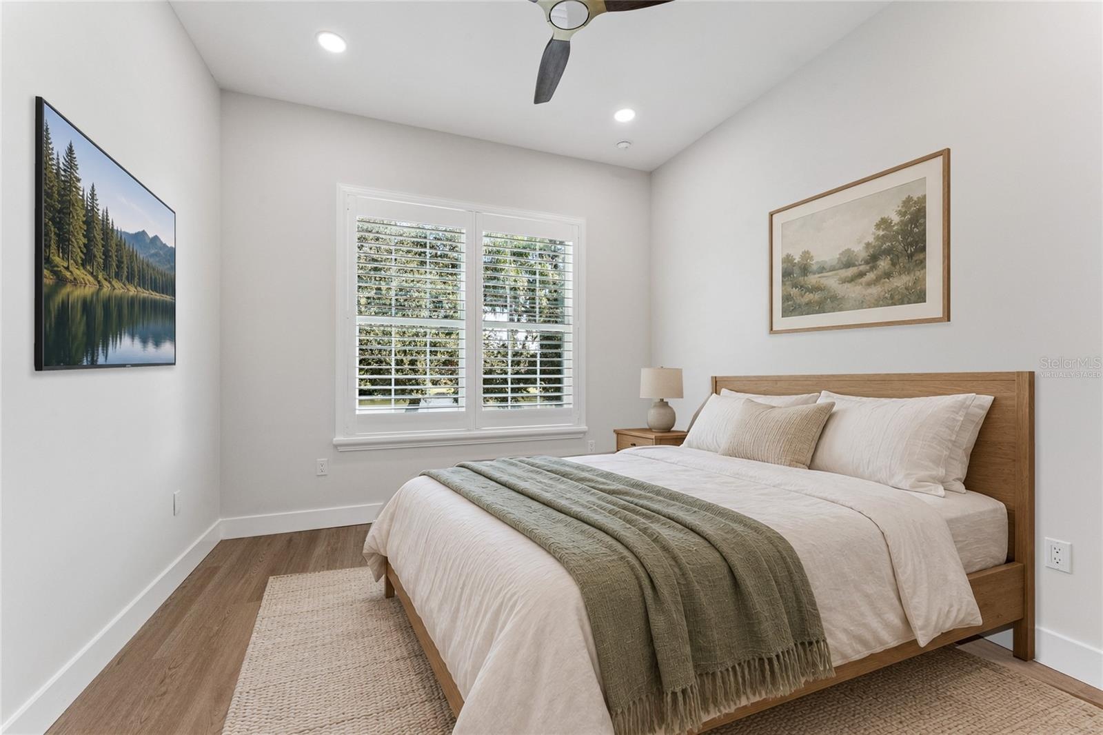Virtually Staged - A shuttered window, ceiling fan, and light walls create a bright bedroom setting.