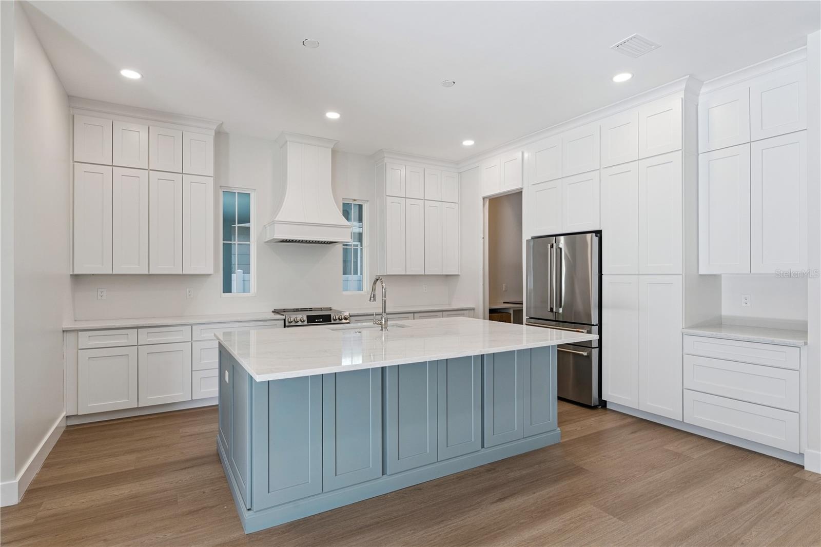 The main kitchen features a blue island, white cabinetry, a statement range hood, and stainless steel appliances.
