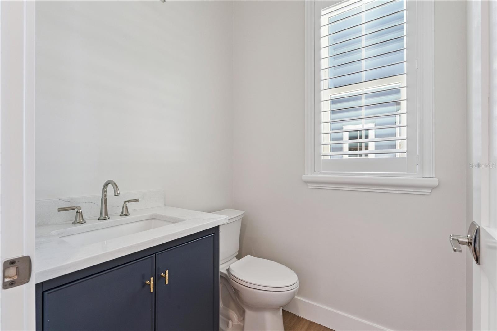 A navy vanity, light countertop, and shuttered window give this powder room a crisp finish.