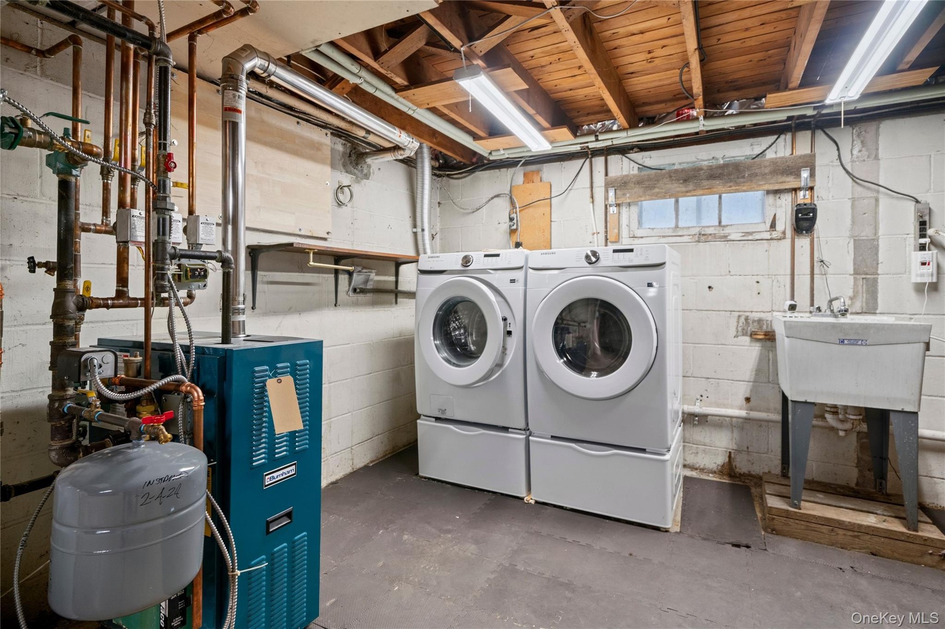 The right side of the stairs has the laundry area with newer Samsung front-load washer (2022) and a Samsung electric dryer (2023), plus a slop sink.