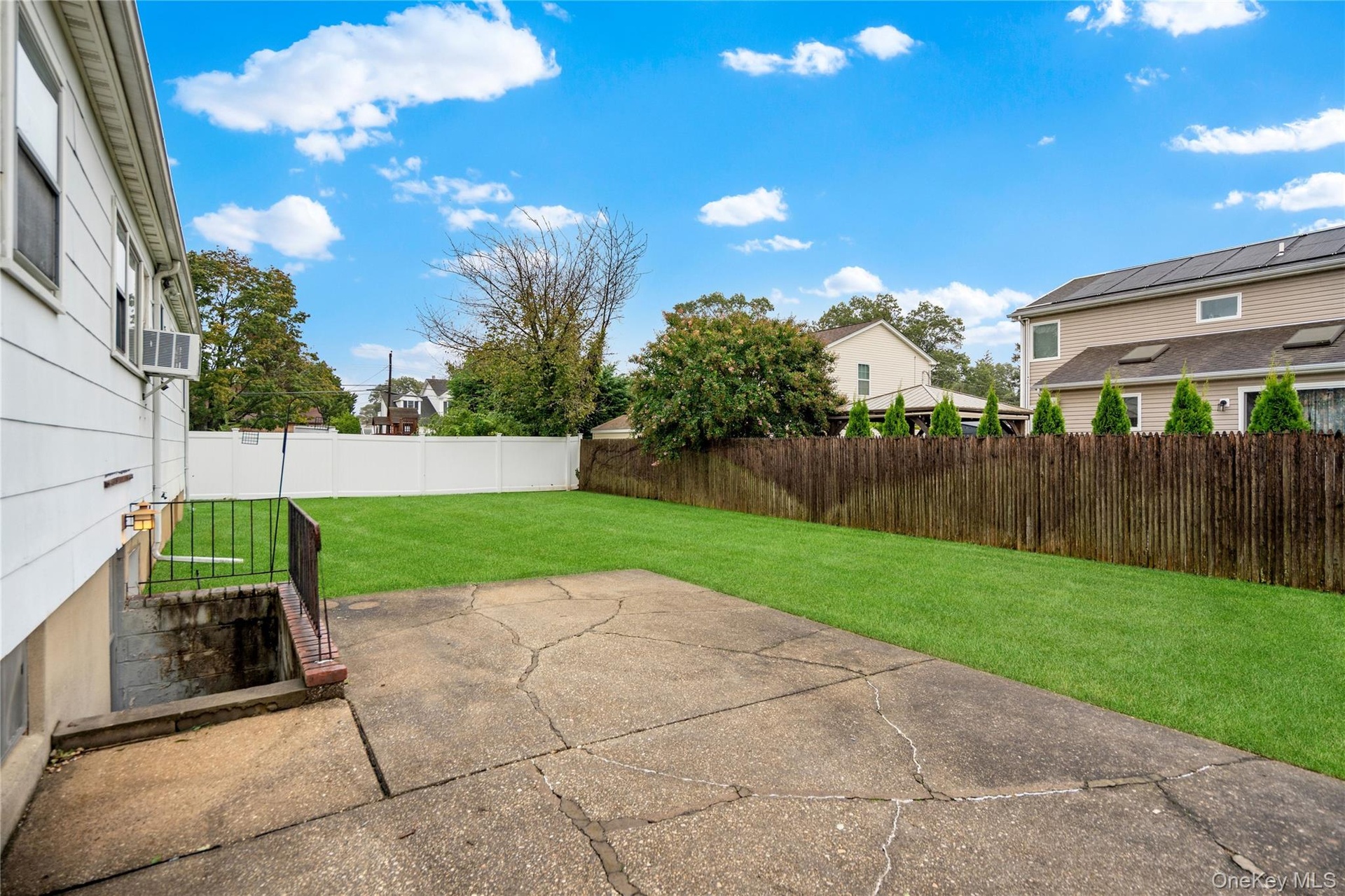 The backyard patio is located off the rear corner of the house and the stairs down to the outside entrance of the basement.