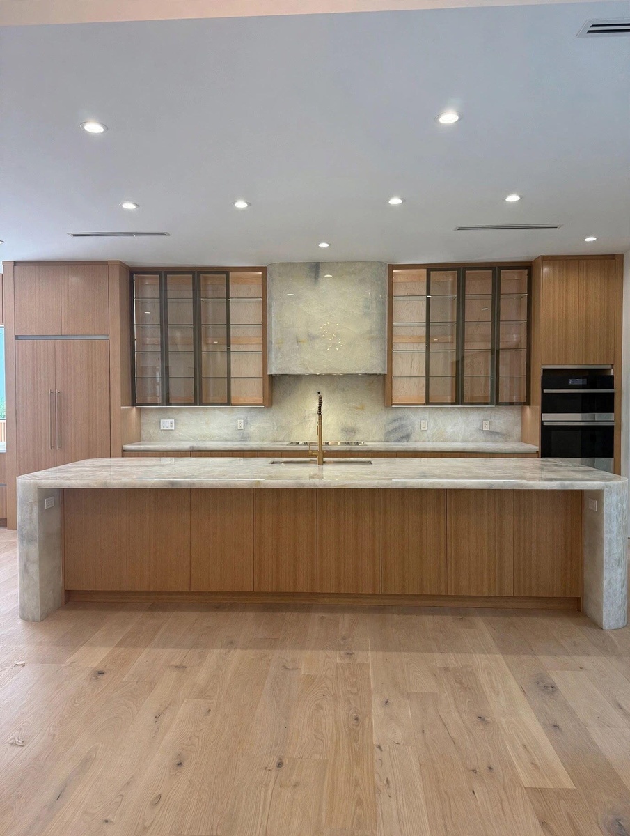 Wide plank wood-finish flooring, recessed lighting, and a kitchen island with stone waterfall edges