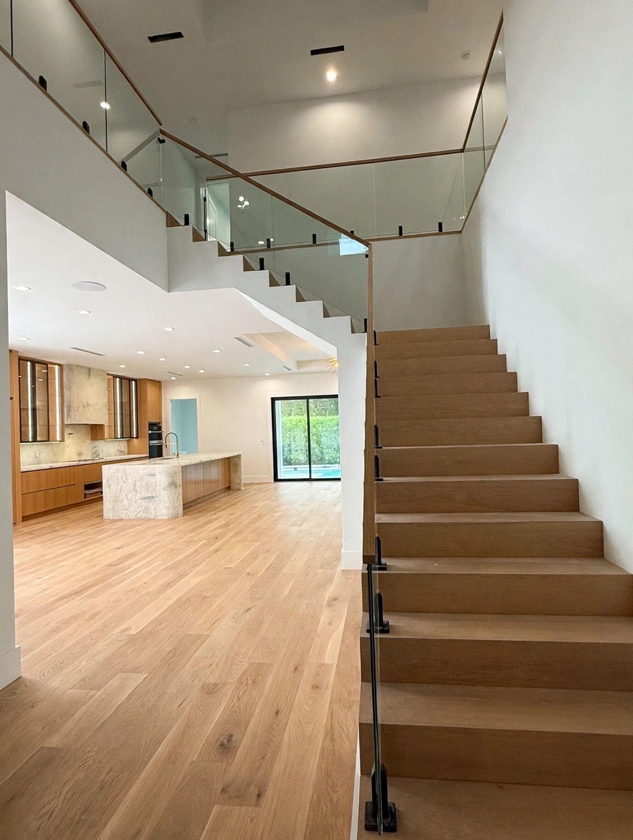 Floating wood staircase with glass railing and wood handrail, hardwood flooring, recessed lighting, and a kitchen featuring a stone-clad island