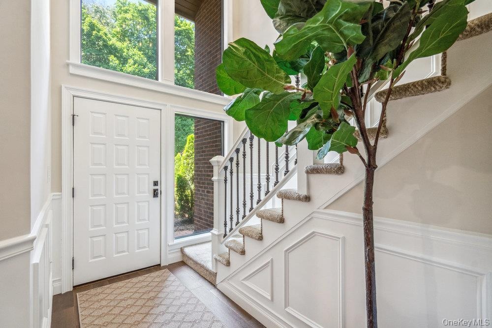 Two-story entry with transom and sidelight windows, a paneled white door, and a staircase featuring a wrought iron railing and carpeted treads