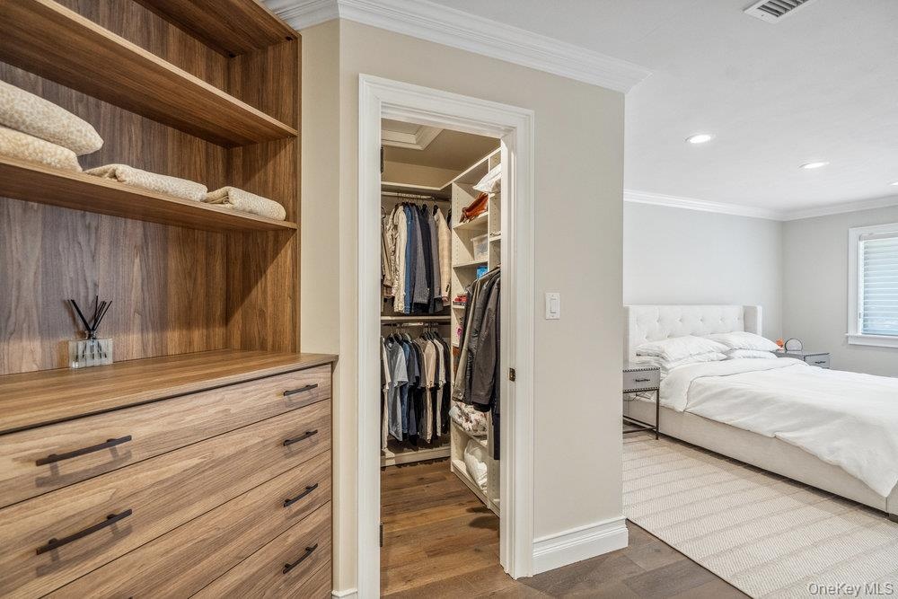 Built-in wood-finish shelving and drawers, walk-in closet with custom organization, crown molding, recessed lighting, and wood-finish flooring