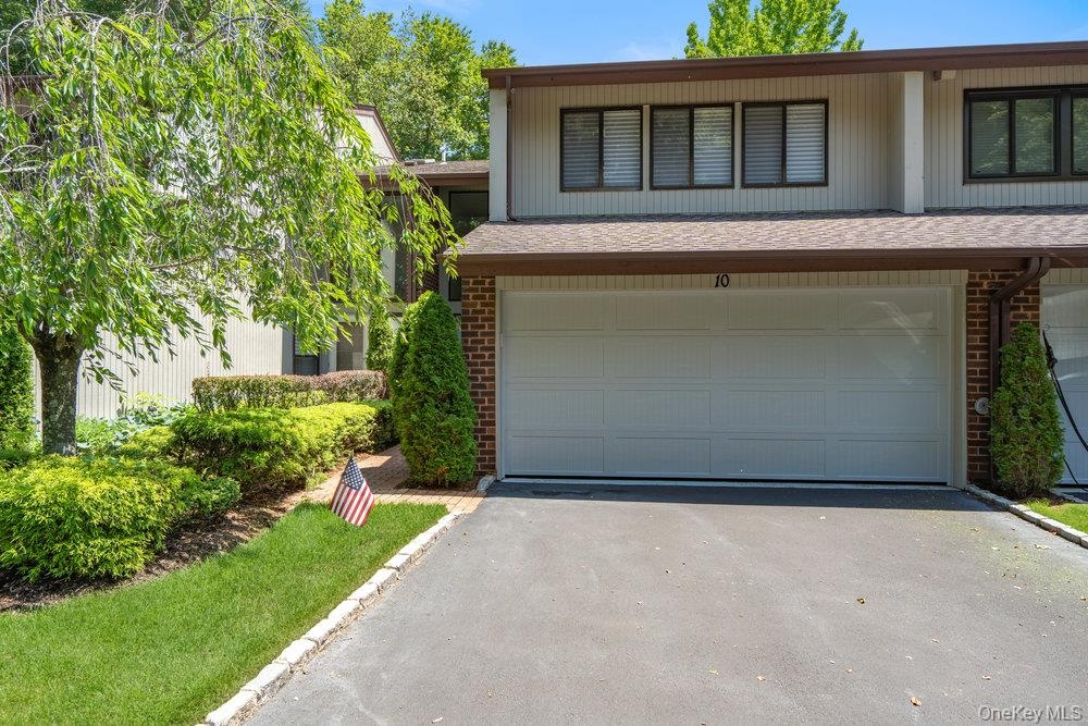 Attached two-car garage, asphalt driveway, brick facade accents, and mature landscaping