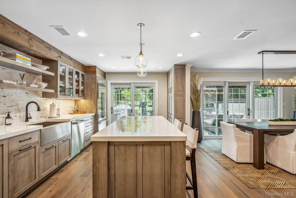 Modern kitchen featuring a large central island, light wood-finish cabinetry, stainless steel appliances, and a farmhouse sink
