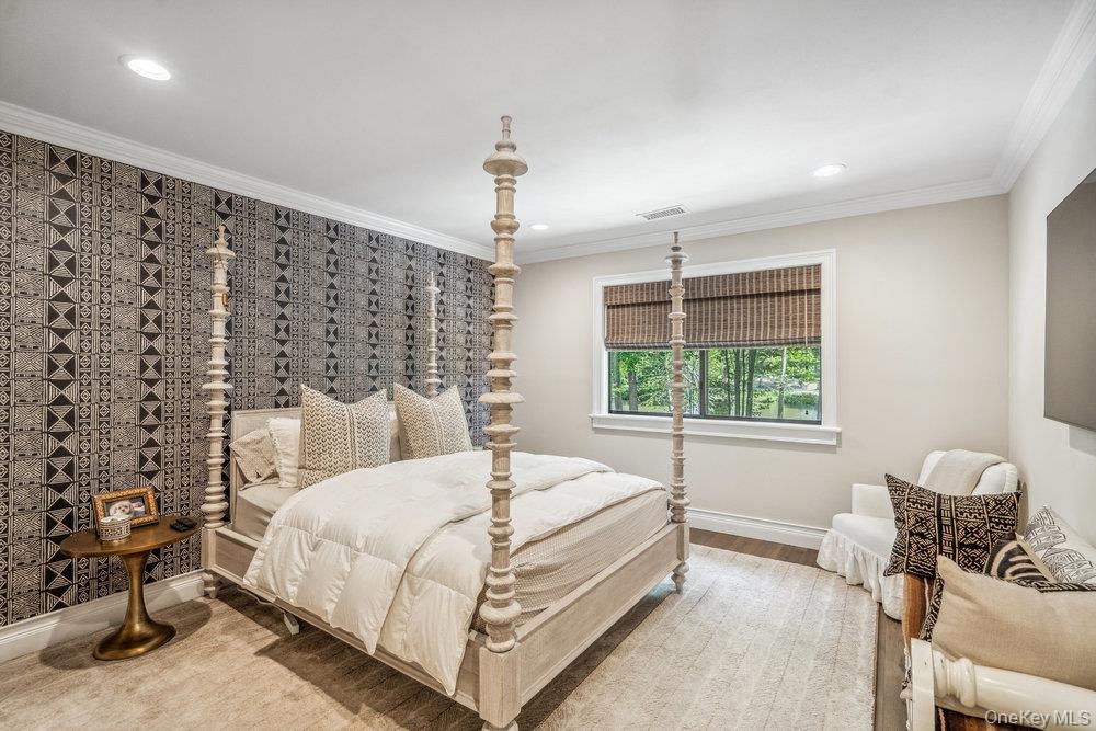 Recessed lighting, crown molding, patterned accent wall, wood-finish flooring, and a large window with privacy shades